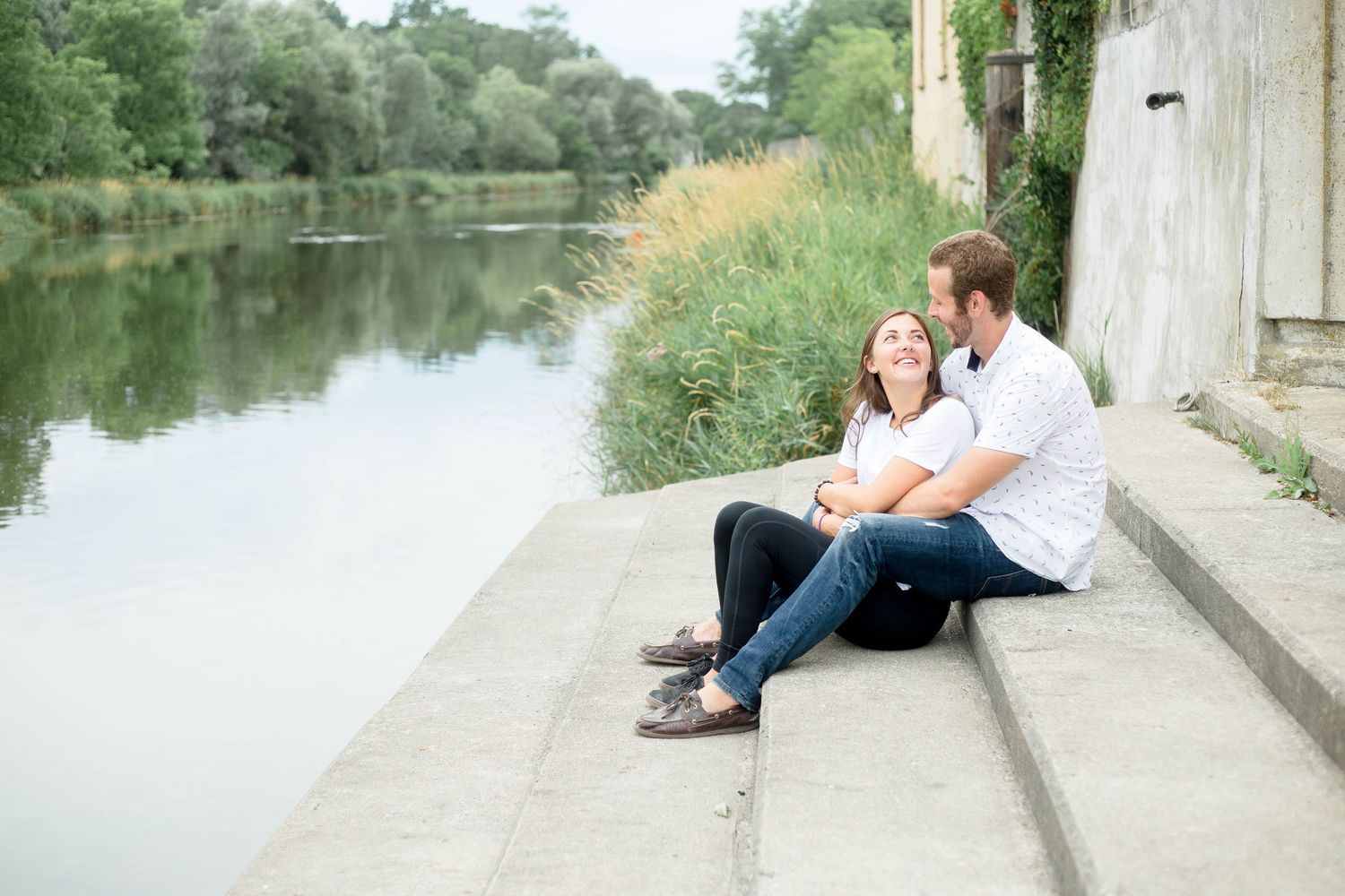 Couple sitting on concrete steps by a calm river smiling together.
