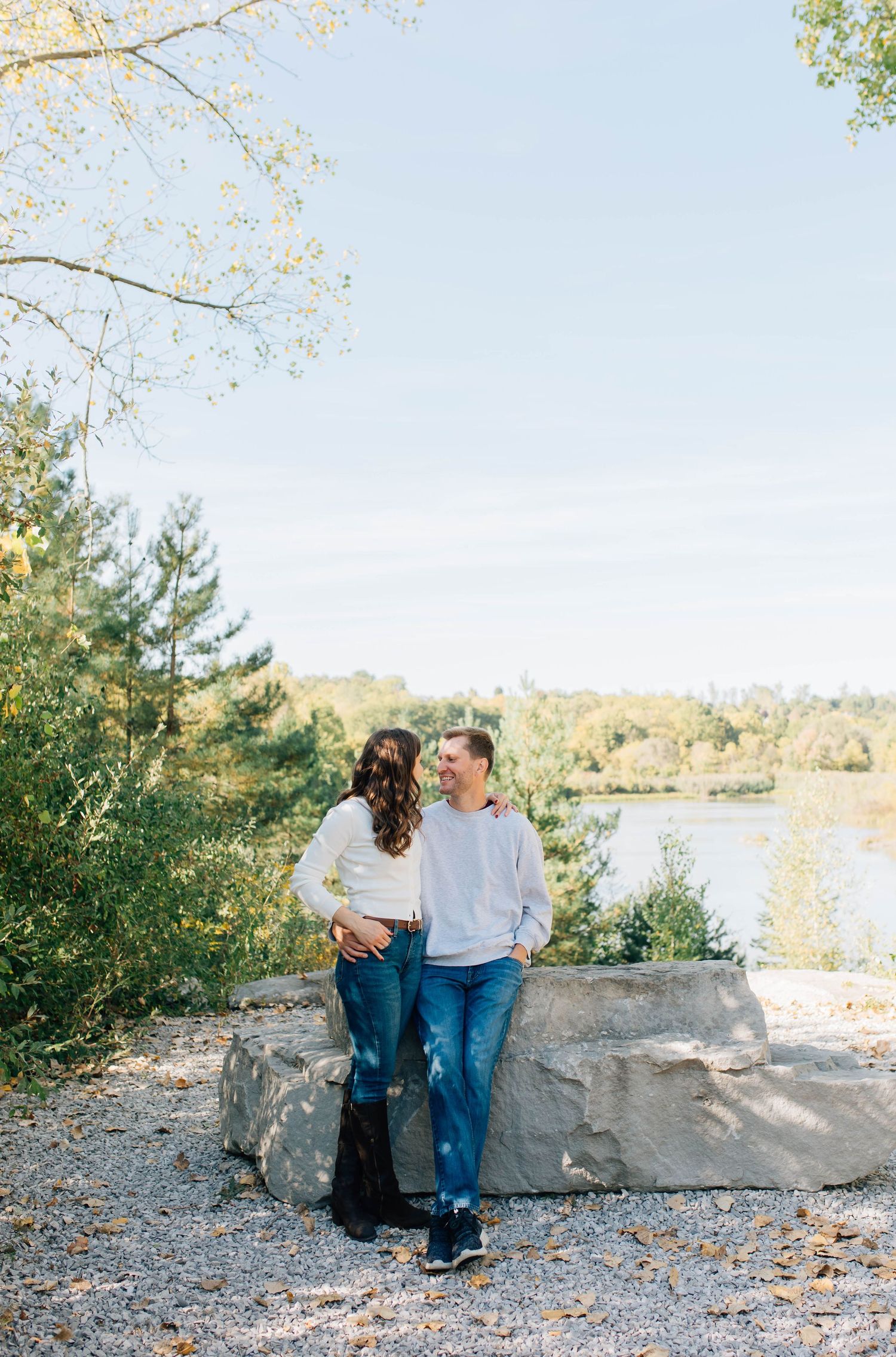 Couple leaning on large rock sharing a moment with a lake and trees behind them.