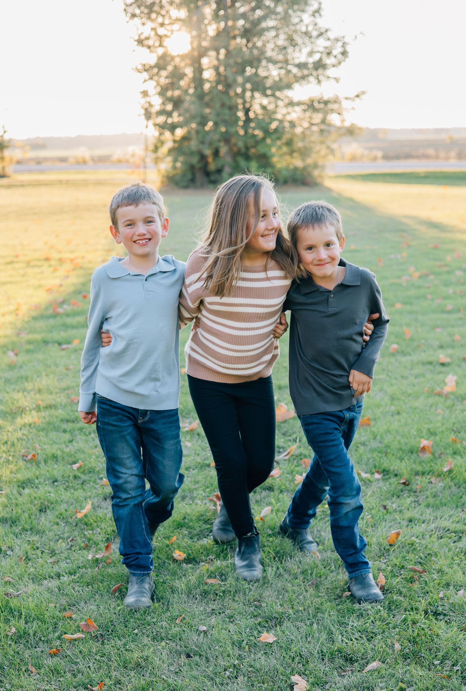 Three siblings smiling and hugging each other during a golden hour outdoor photo session.