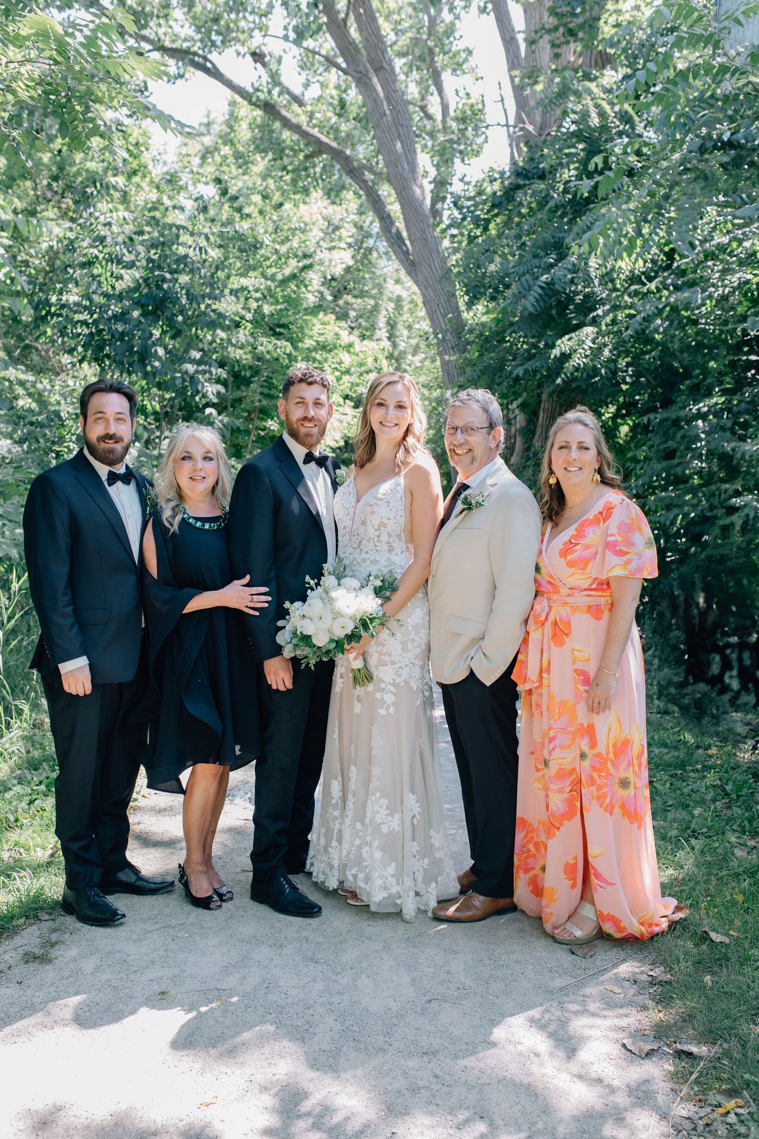 Bride and groom with four family members smiling together on a lush outdoor trail in Paris Ontario.