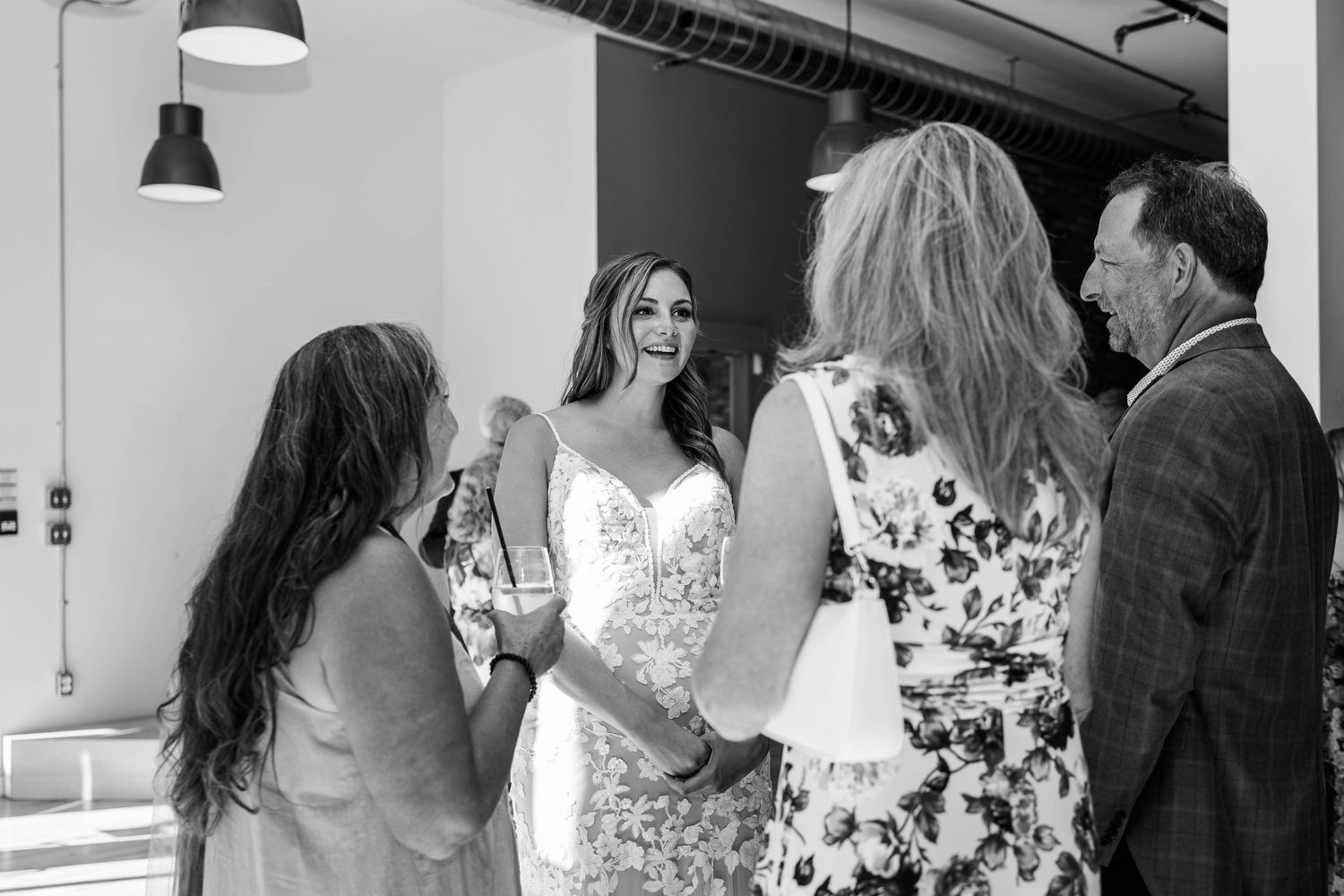 Bride in lace wedding gown laughing with guests during wedding reception in black and white photo.