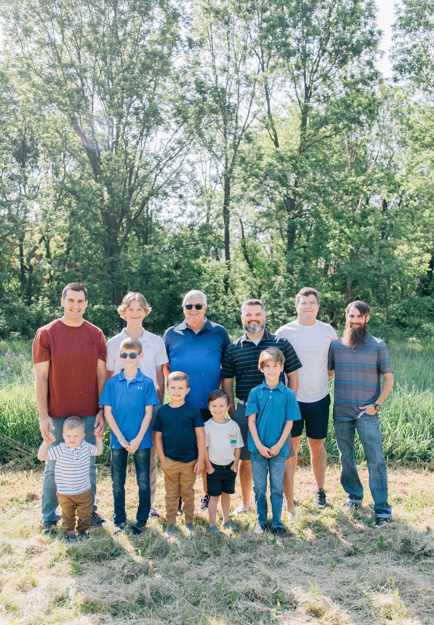 Group of men and boys posing together outdoors in a lush green park for a family photo.