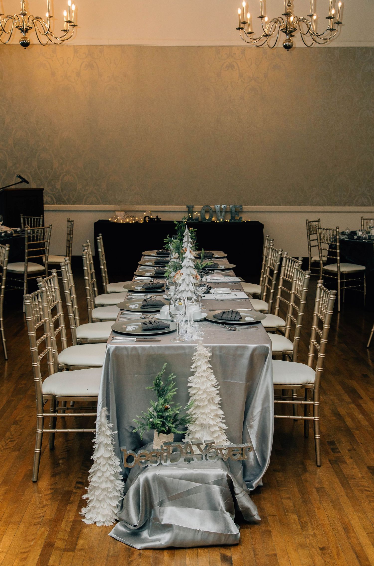 Elegant winter wedding head table with silver satin linen, white feather trees, and gold chiavari chairs.