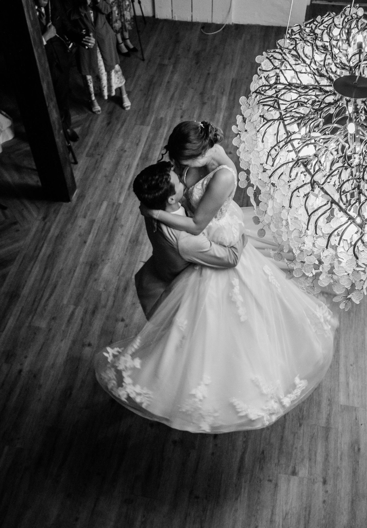 Black and white aerial shot of groom lifting bride during romantic first dance at reception.