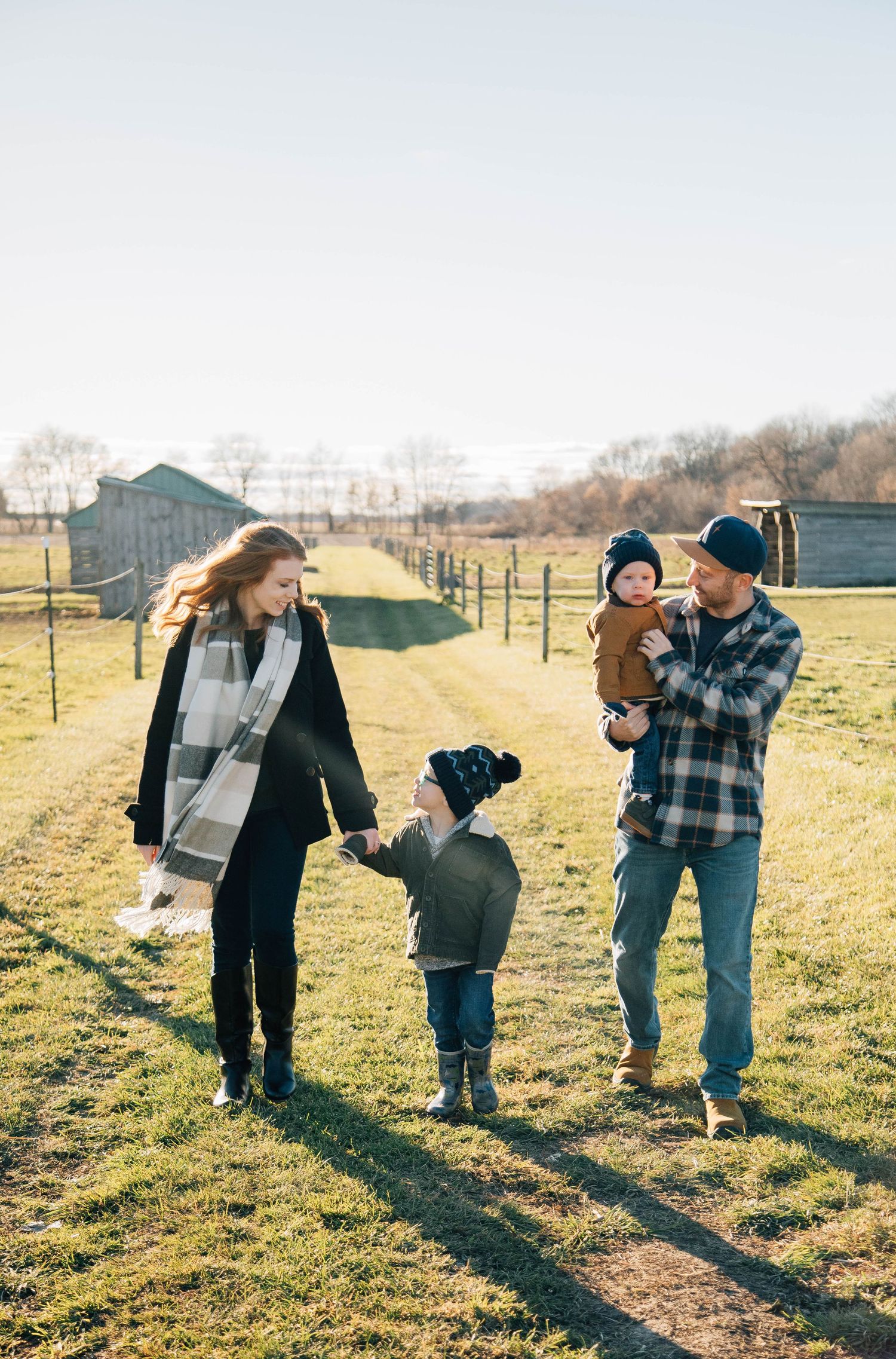 A young family of four walks together in a sunny farm field during a fall outdoor family portrait session.