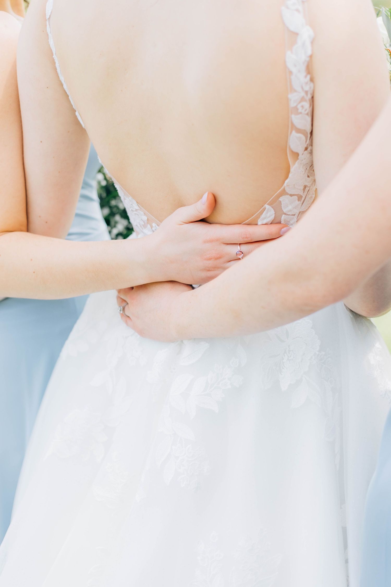 Close-up of bridesmaids hands gently embracing the open lace back of the brides elegant wedding gown.