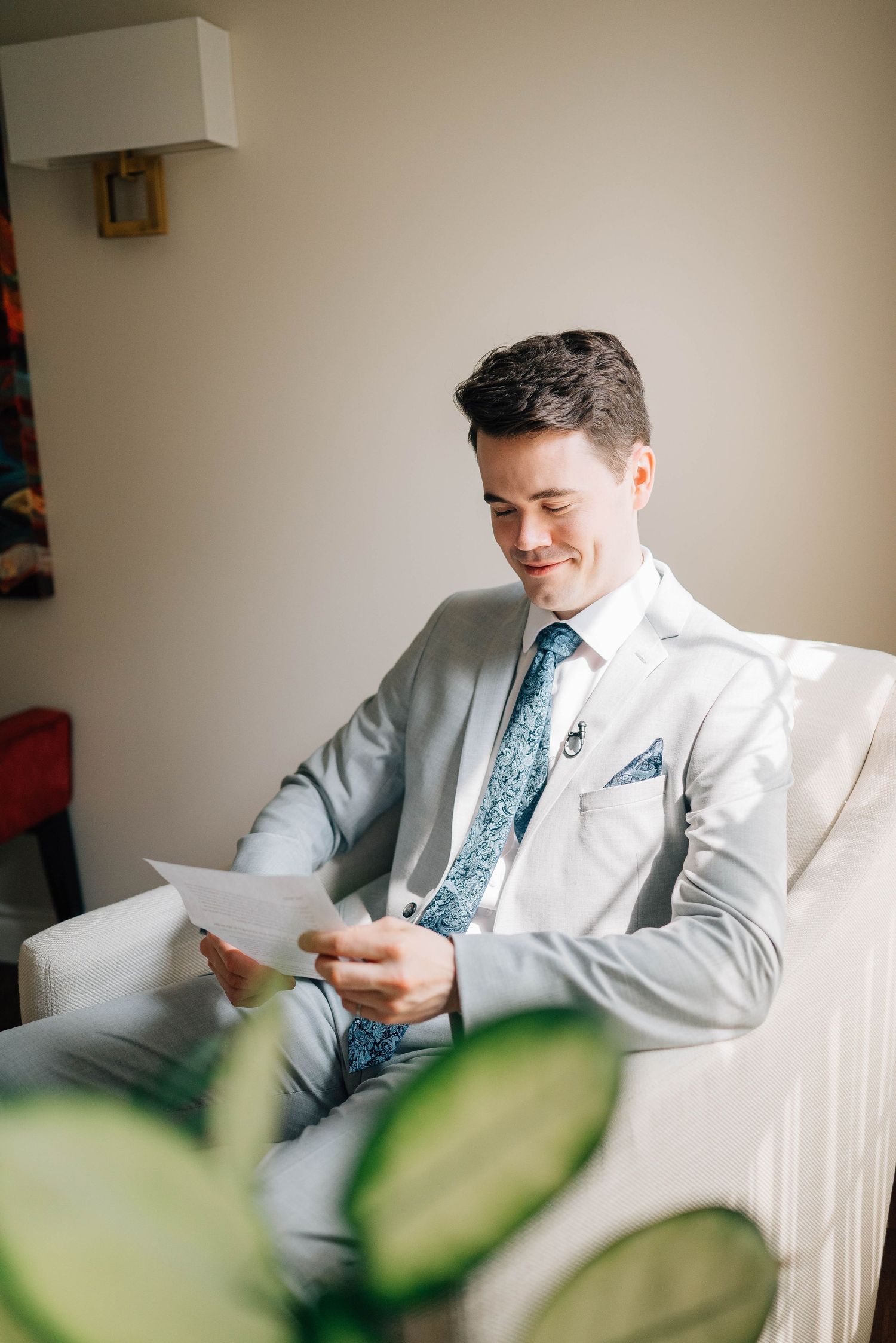 Handsome groom in gray suit smiles while reading a heartfelt letter before the wedding.