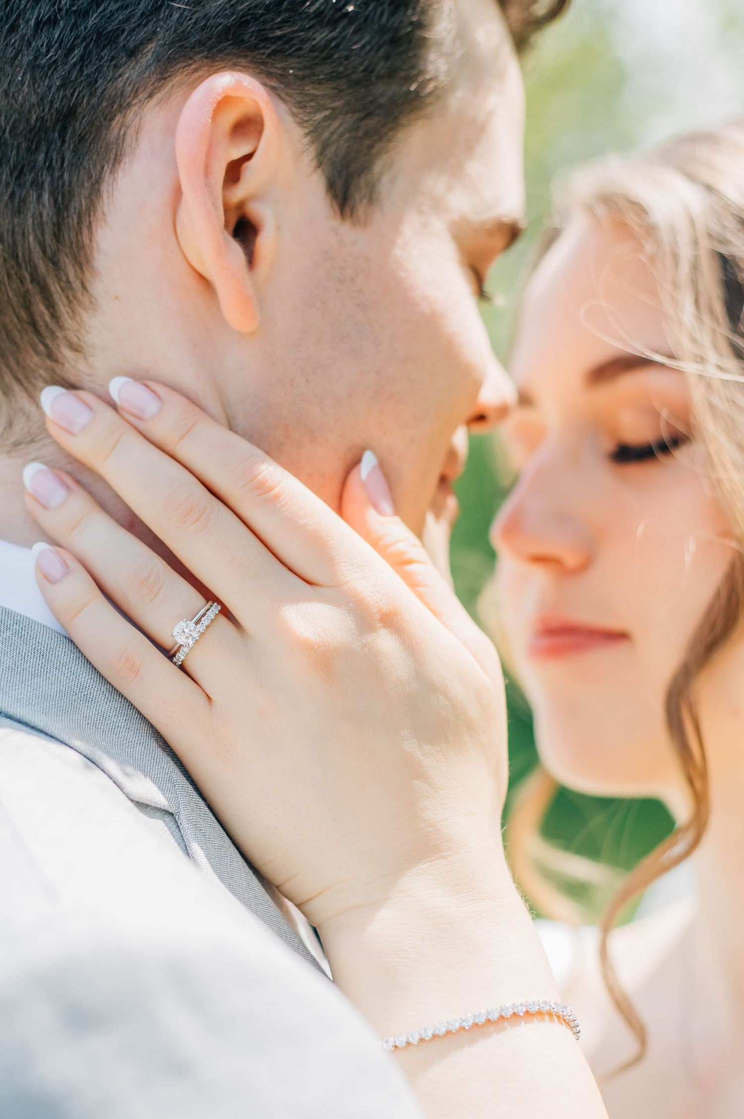 Close-up of bride touching grooms face with diamond engagement ring and pearl bracelet visible.