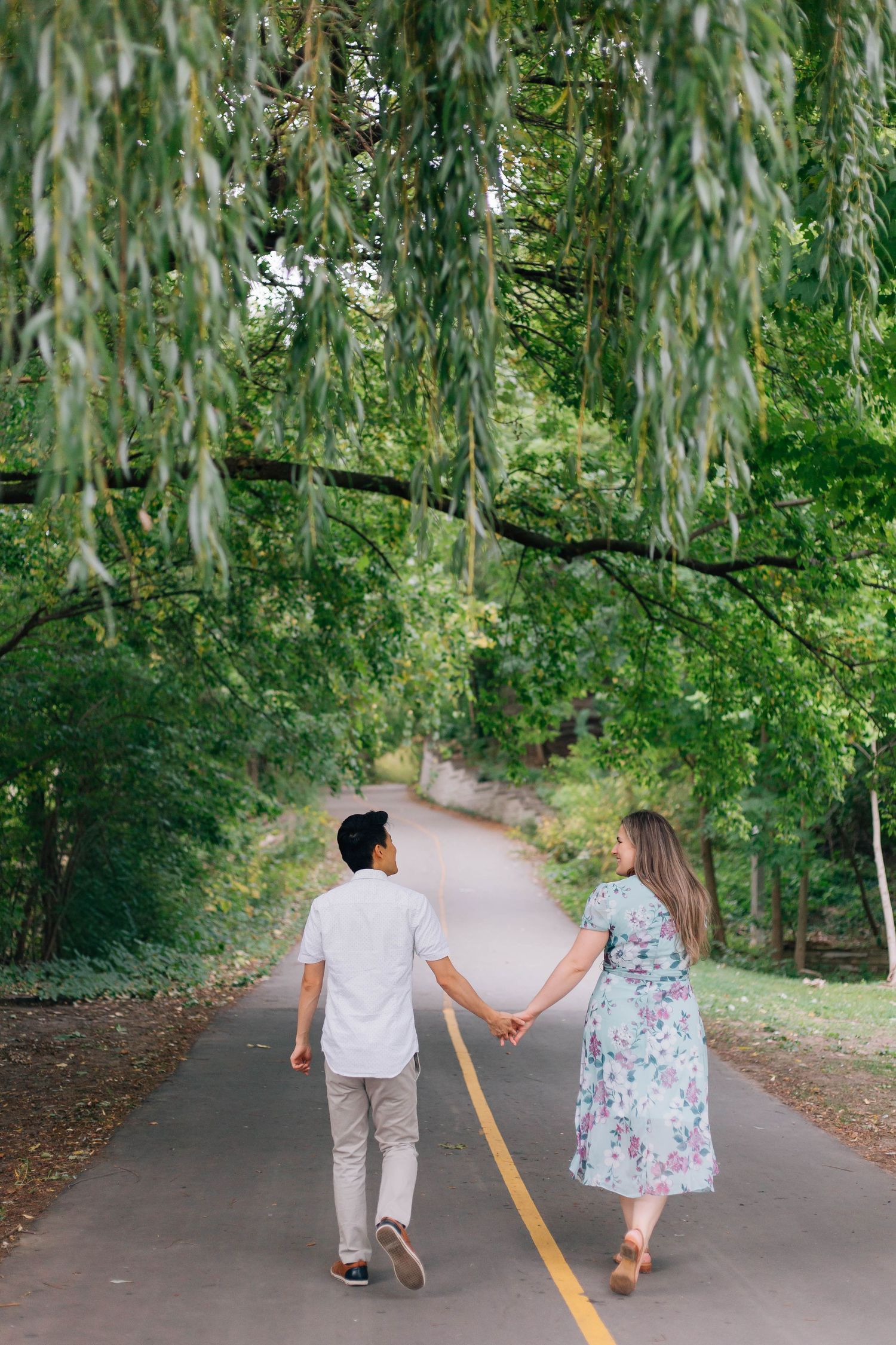 Couple walking away holding hands along a trail in London Ontario surrounded by lush trees