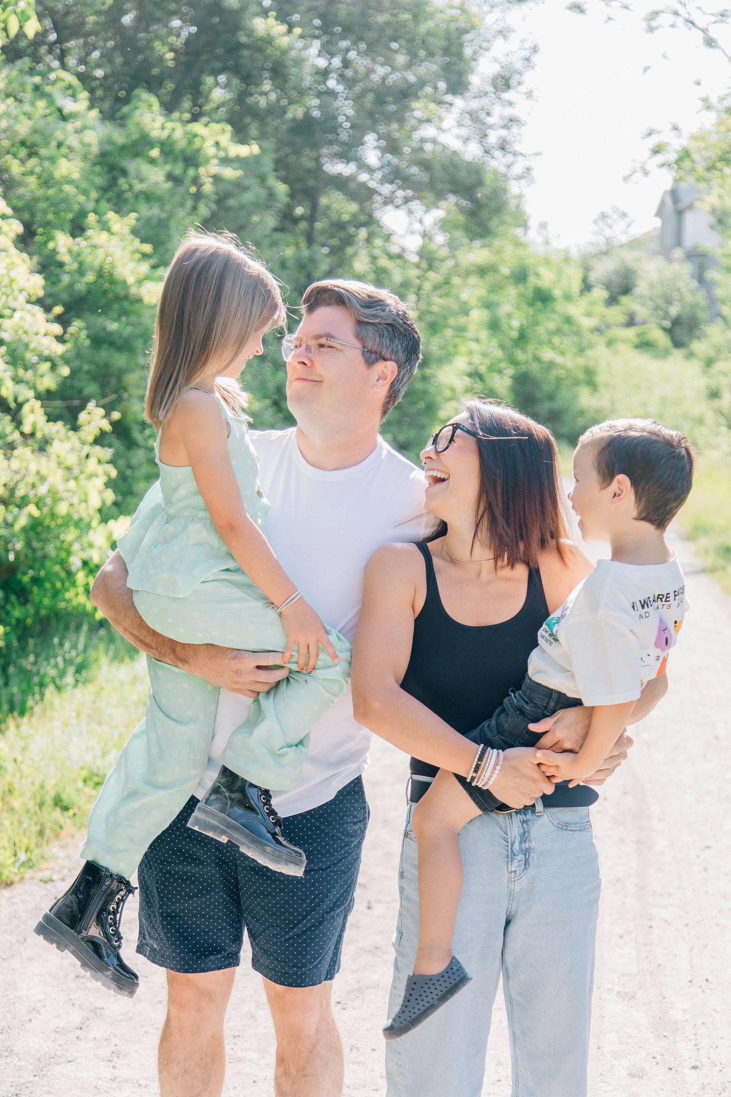 Happy parents holding young daughter and son on sunny outdoor gravel path.