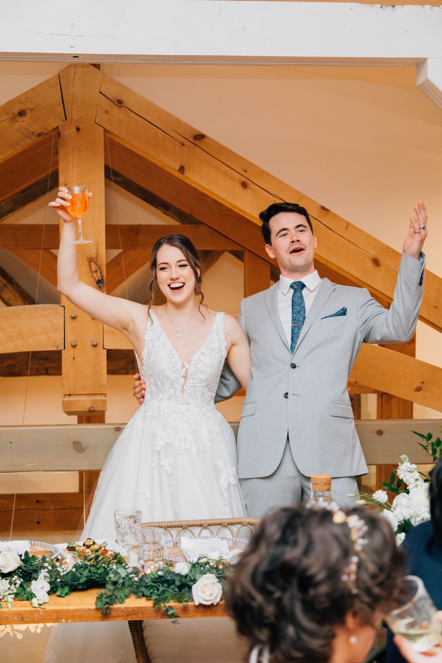Happy bride and groom raising their hands in celebration at their wedding reception table.