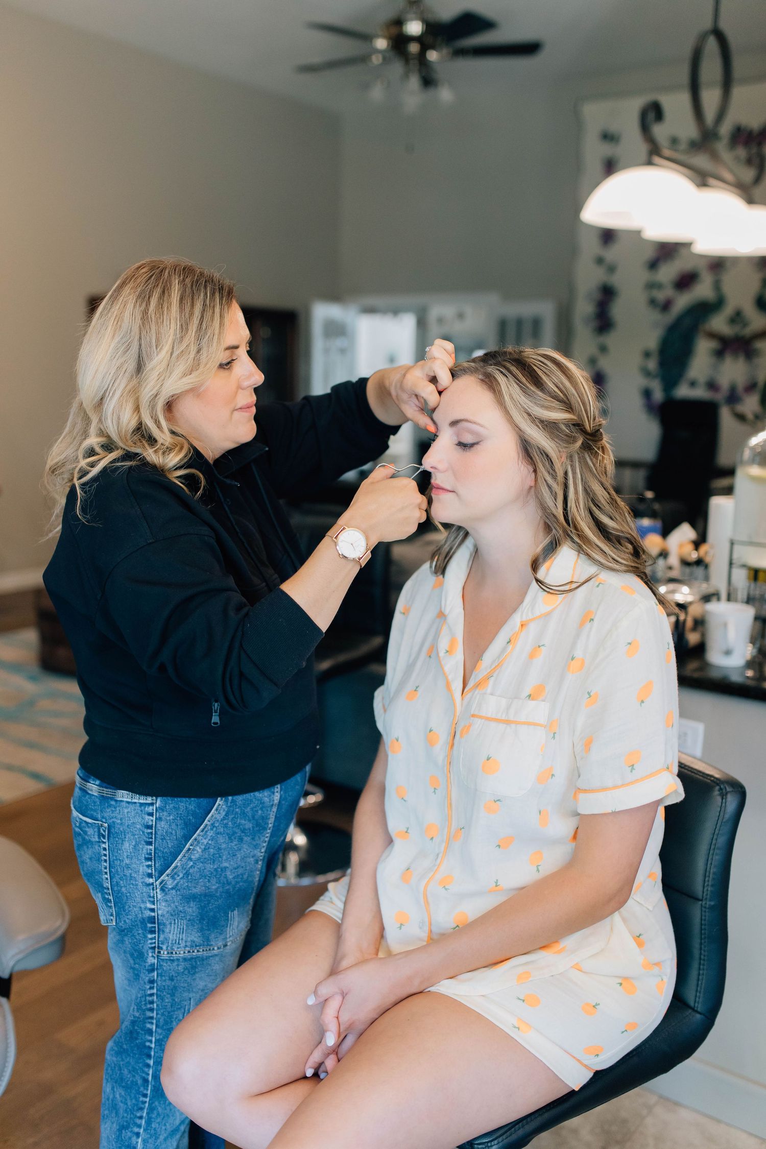 Professional makeup artist applying makeup to bride wearing yellow floral pajamas.