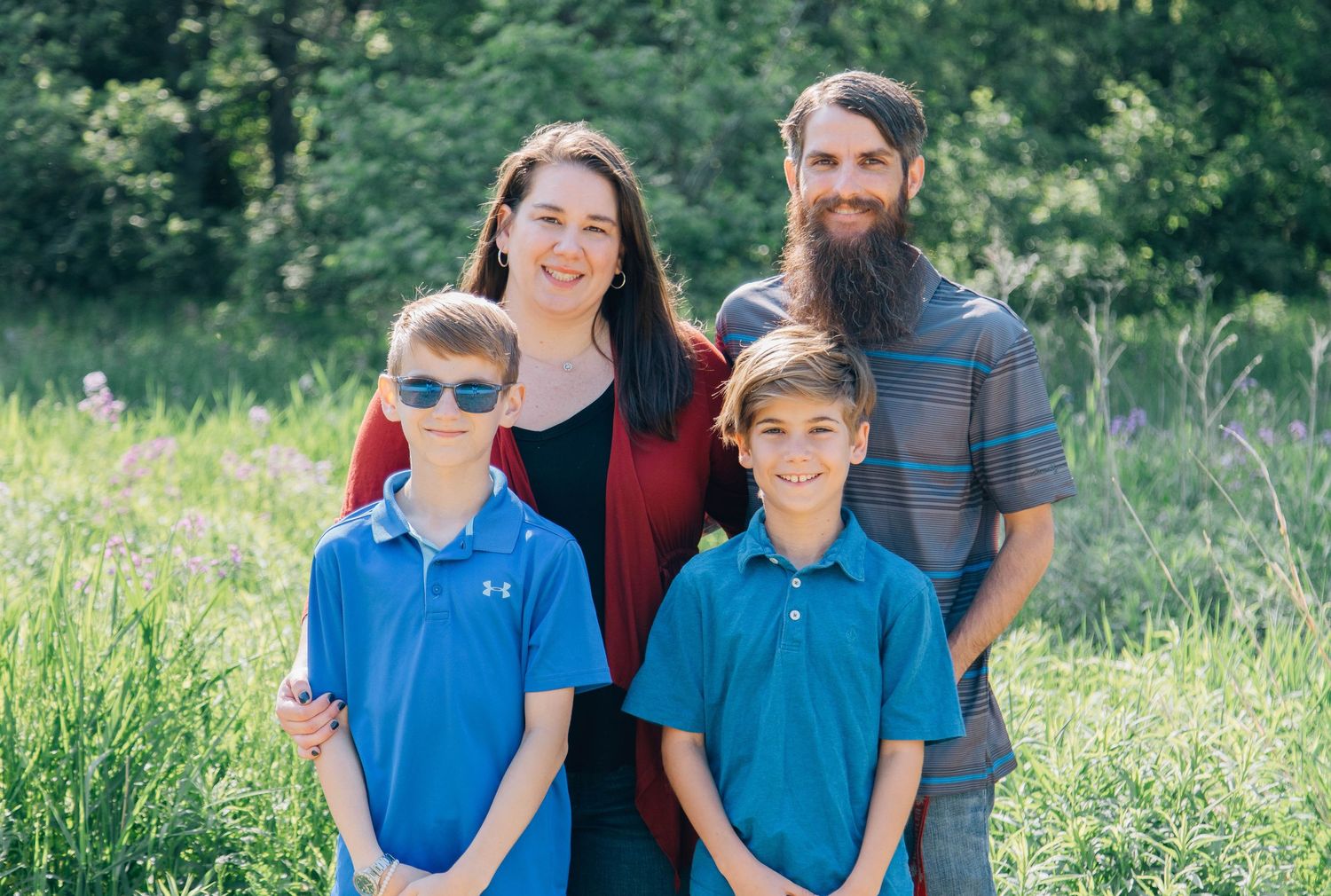 Family of four with bearded dad and two boys in blue polo shirts smiling in a green field.