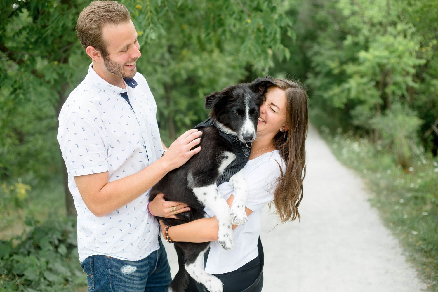 Couple sharing a joyful moment holding their Border Collie dog on a peaceful nature trail surrounded by greenery.