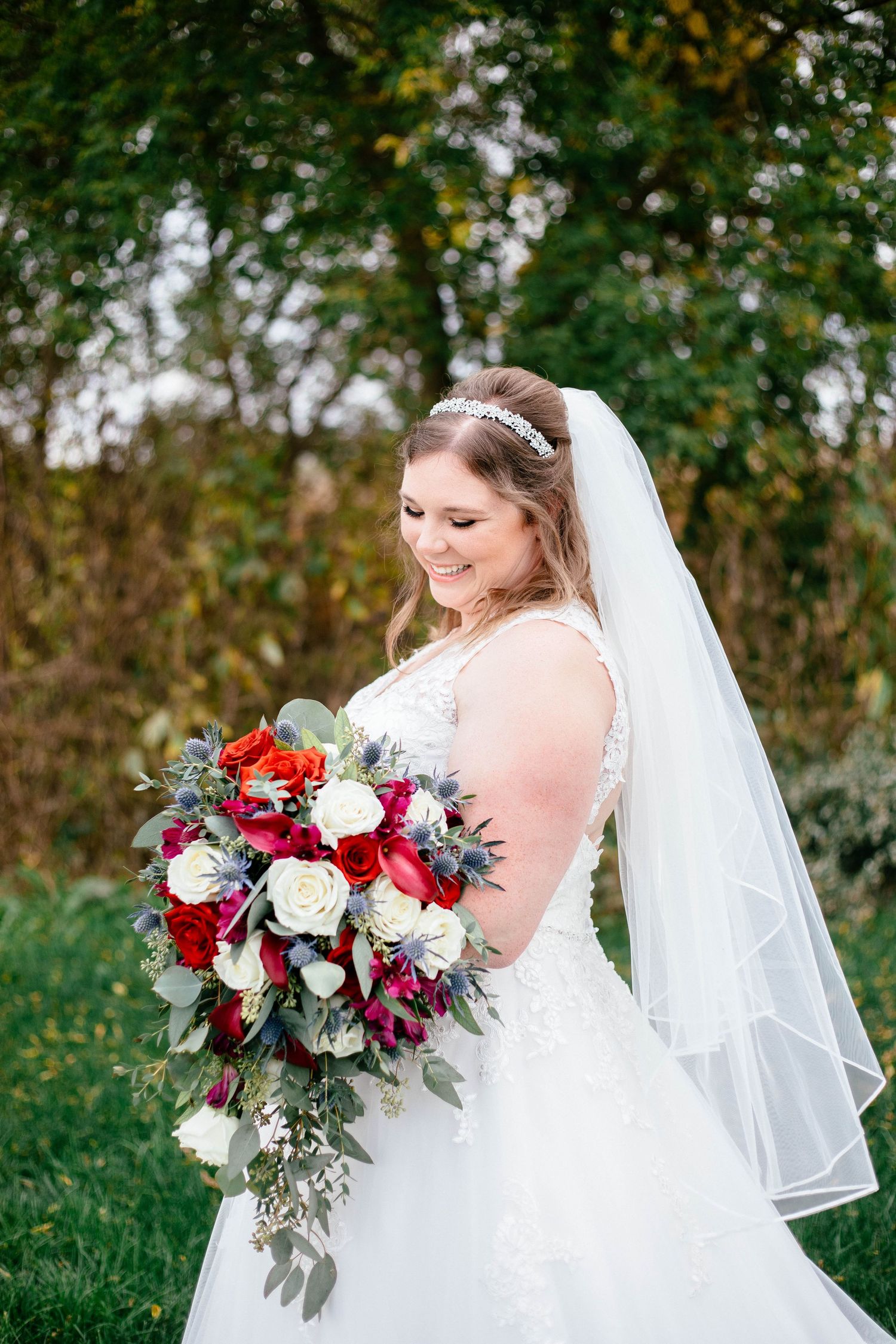 Radiant bride holds a stunning red and white bouquet, wearing a lace wedding gown and tiara veil.