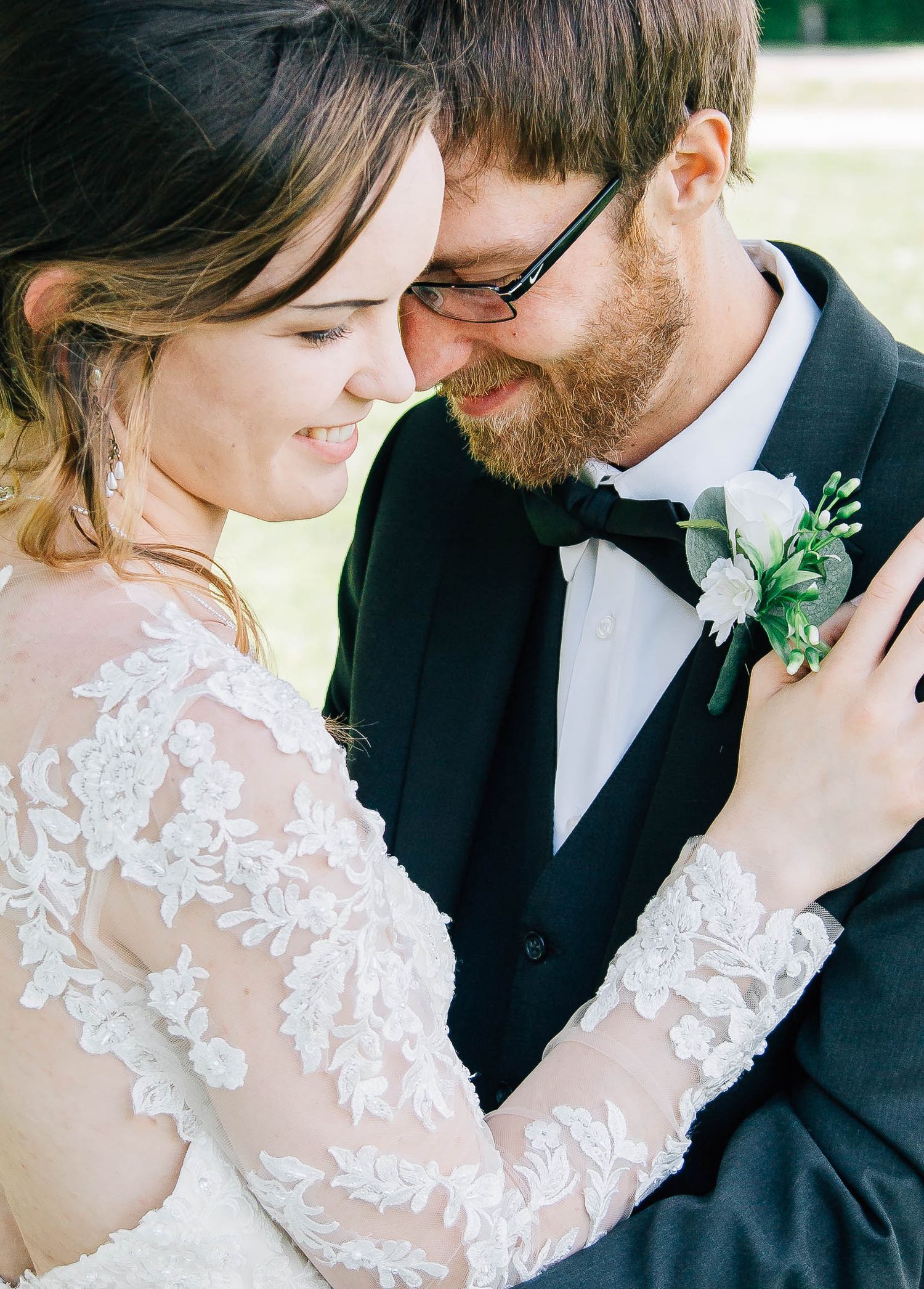 Close-up of smiling bride and groom touching foreheads, groom wearing a white boutonniere.