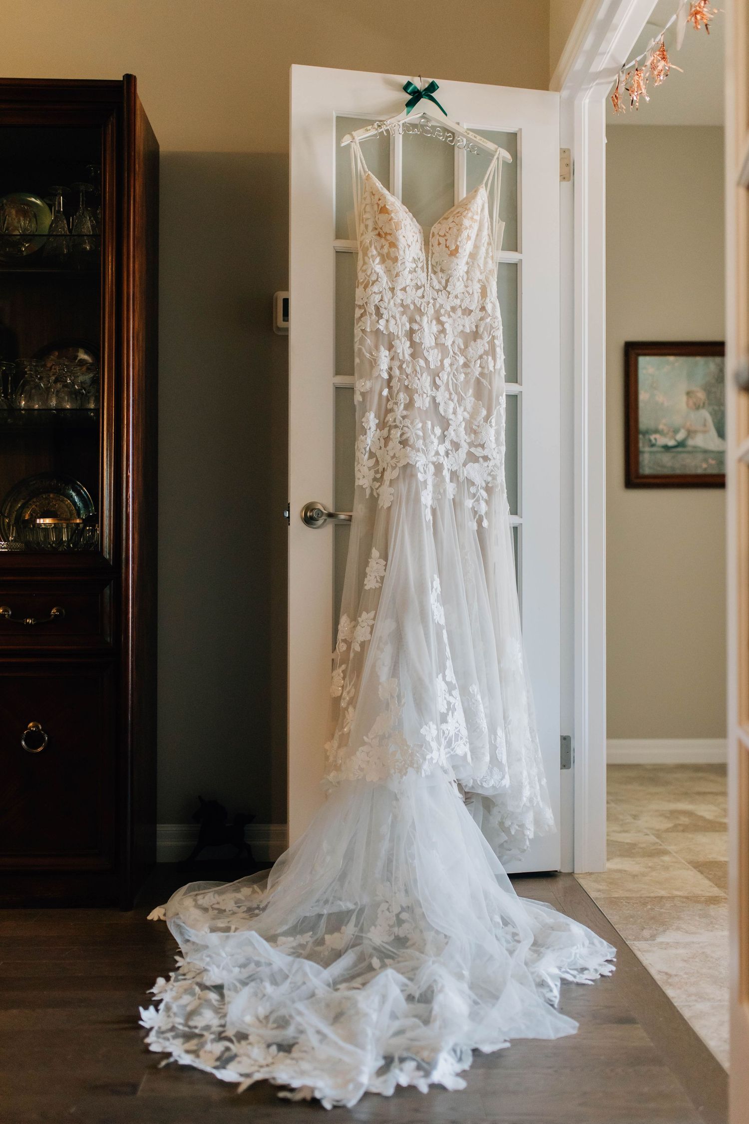 Elegant lace wedding gown with floral appliques hanging on door before ceremony.
