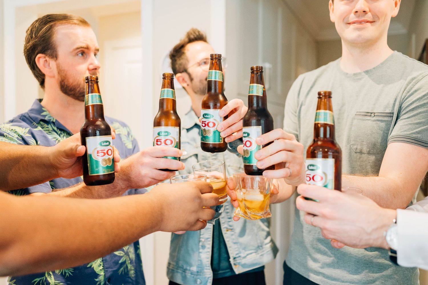 Group of groomsmen toasting with beer bottles and a whiskey glass before a wedding ceremony.