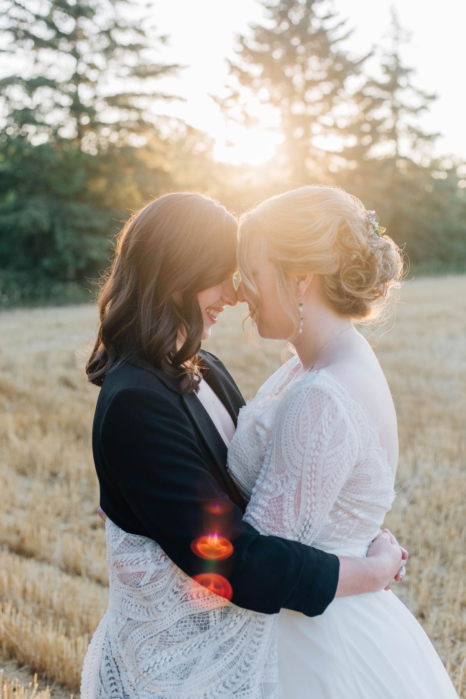 Lesbian wedding couple touching foreheads in a golden wheat field at sunset.