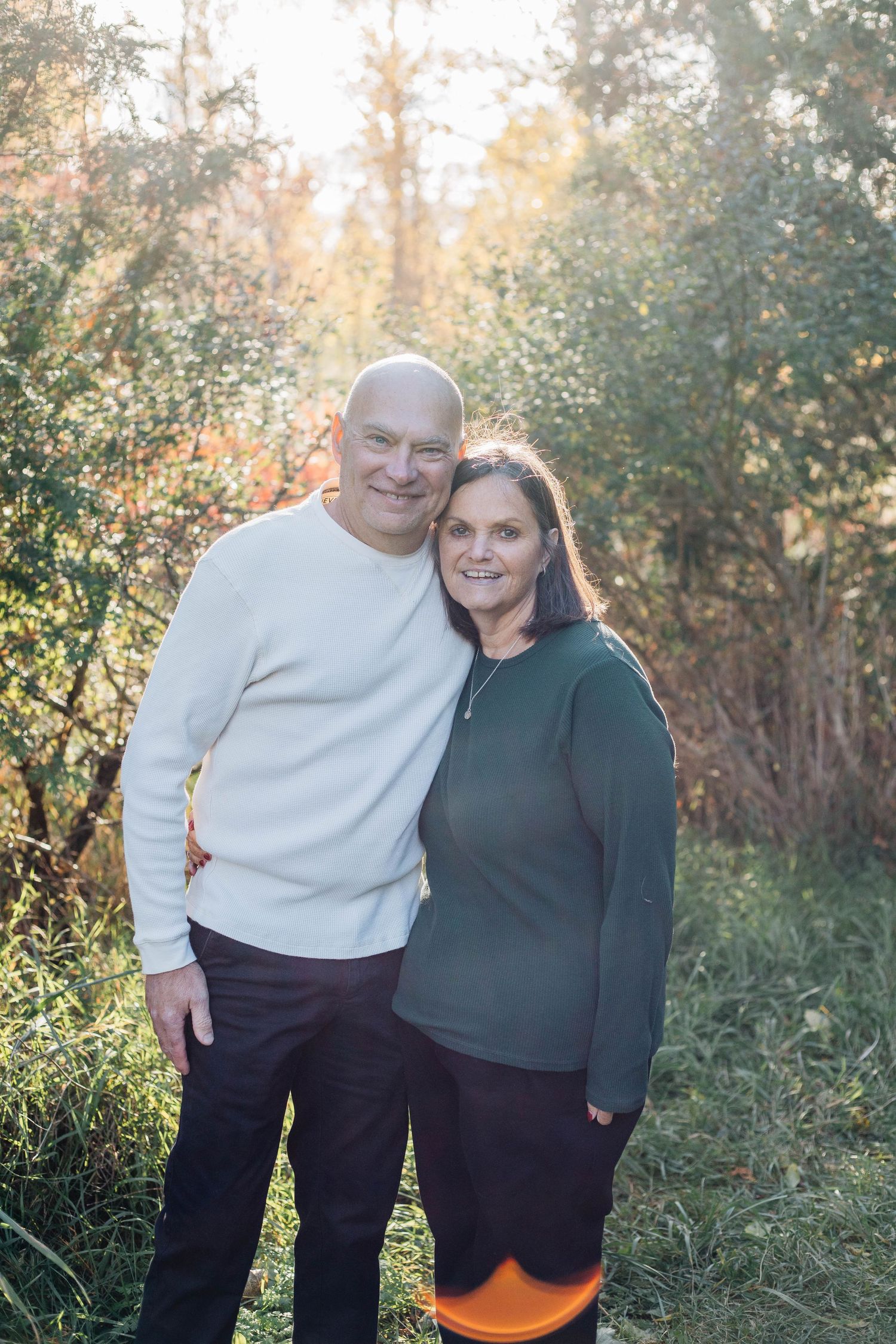 Smiling couple in casual sweaters posing together in a sunny autumn outdoor setting.