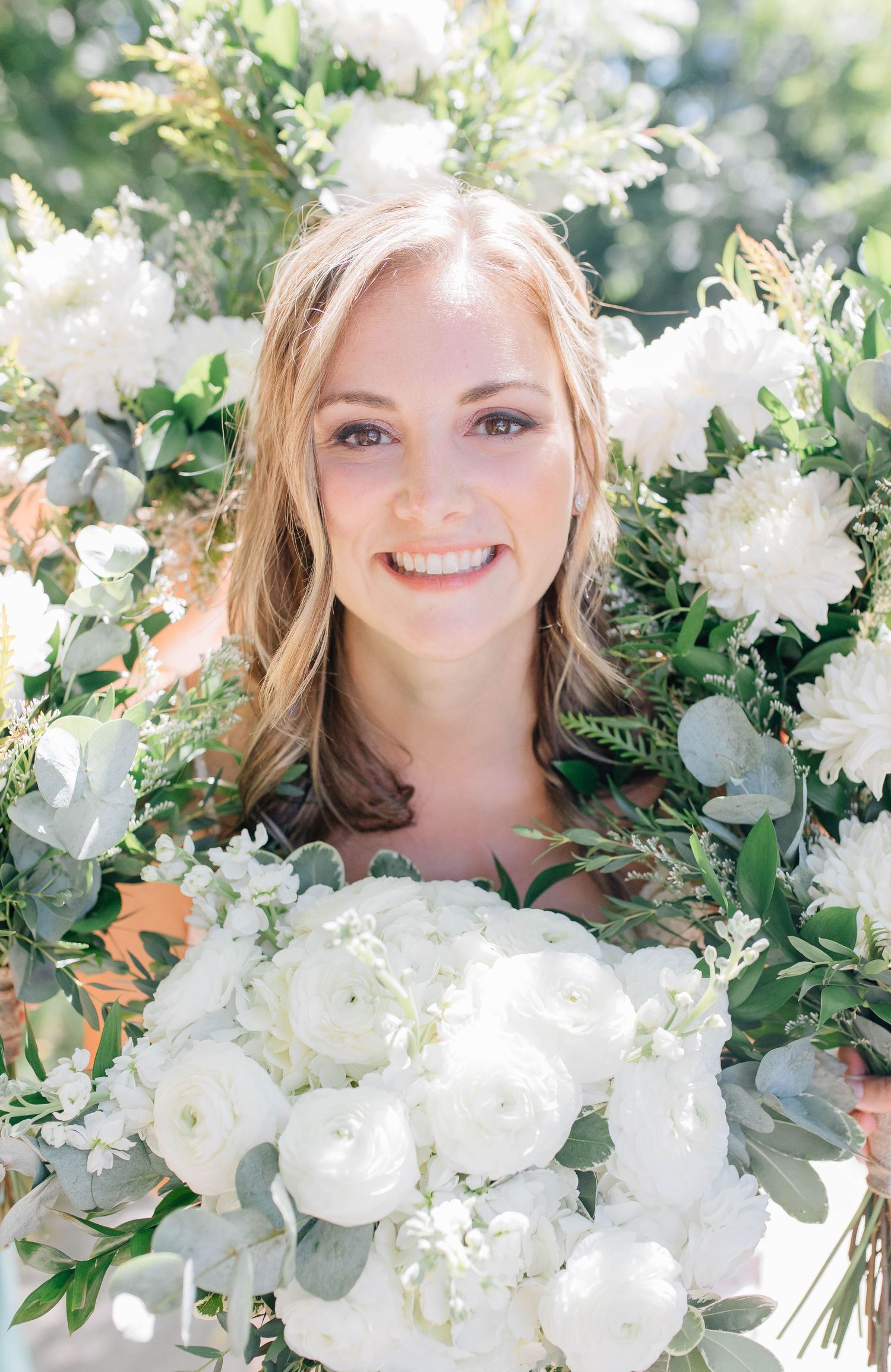 Bride smiling surrounded by lush white floral arrangements and greenery.