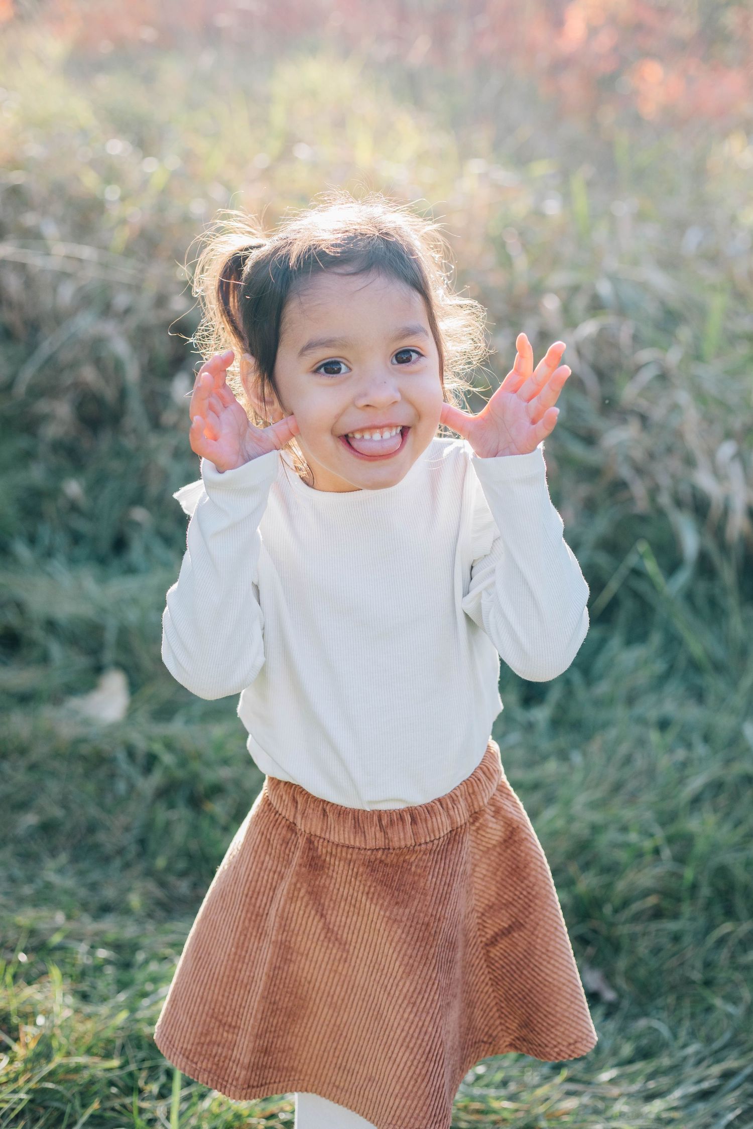 Happy young girl in white top and brown skirt making funny hands gesture in autumn outdoor setting.