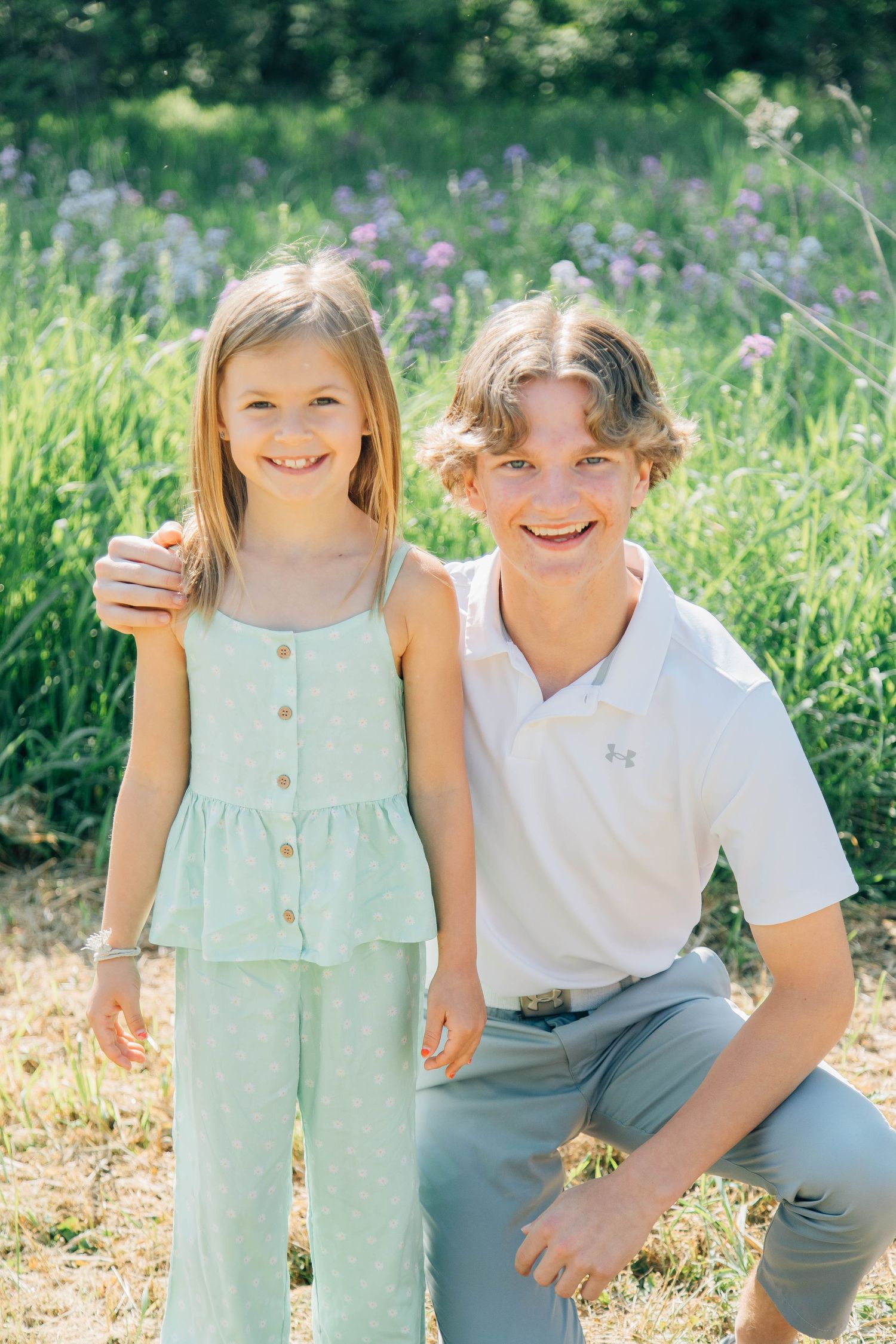 Smiling young girl and teenage boy posing together in a sunny wildflower meadow.