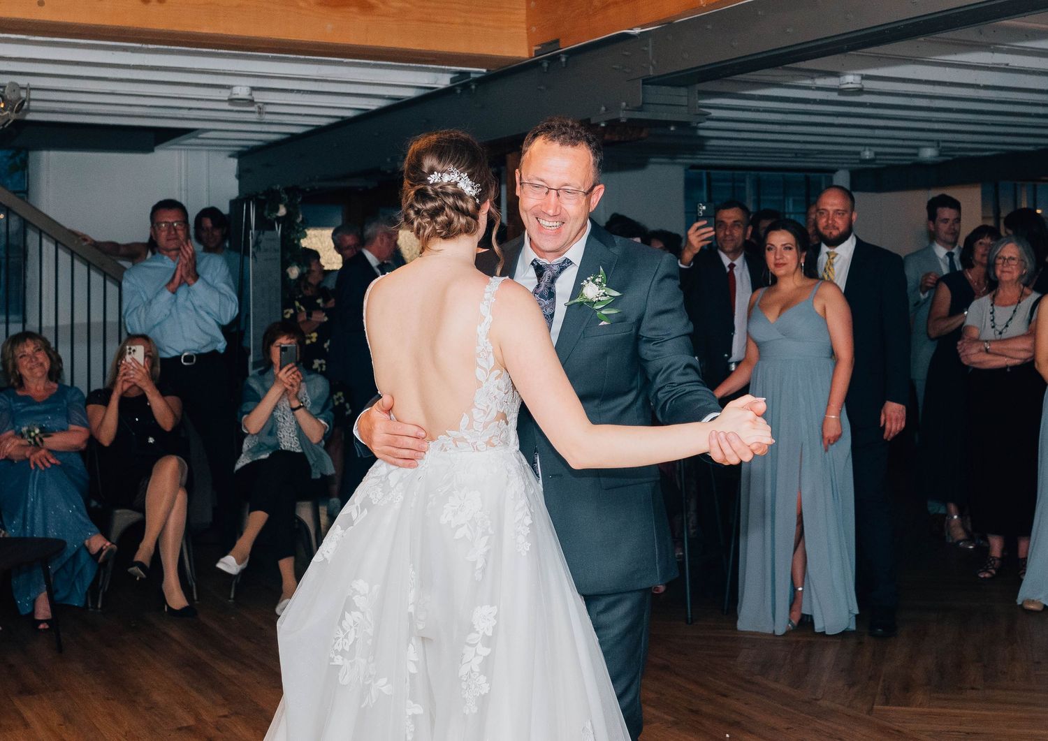 Bride sharing a tender father-daughter dance while wedding guests watch and applaud in background.