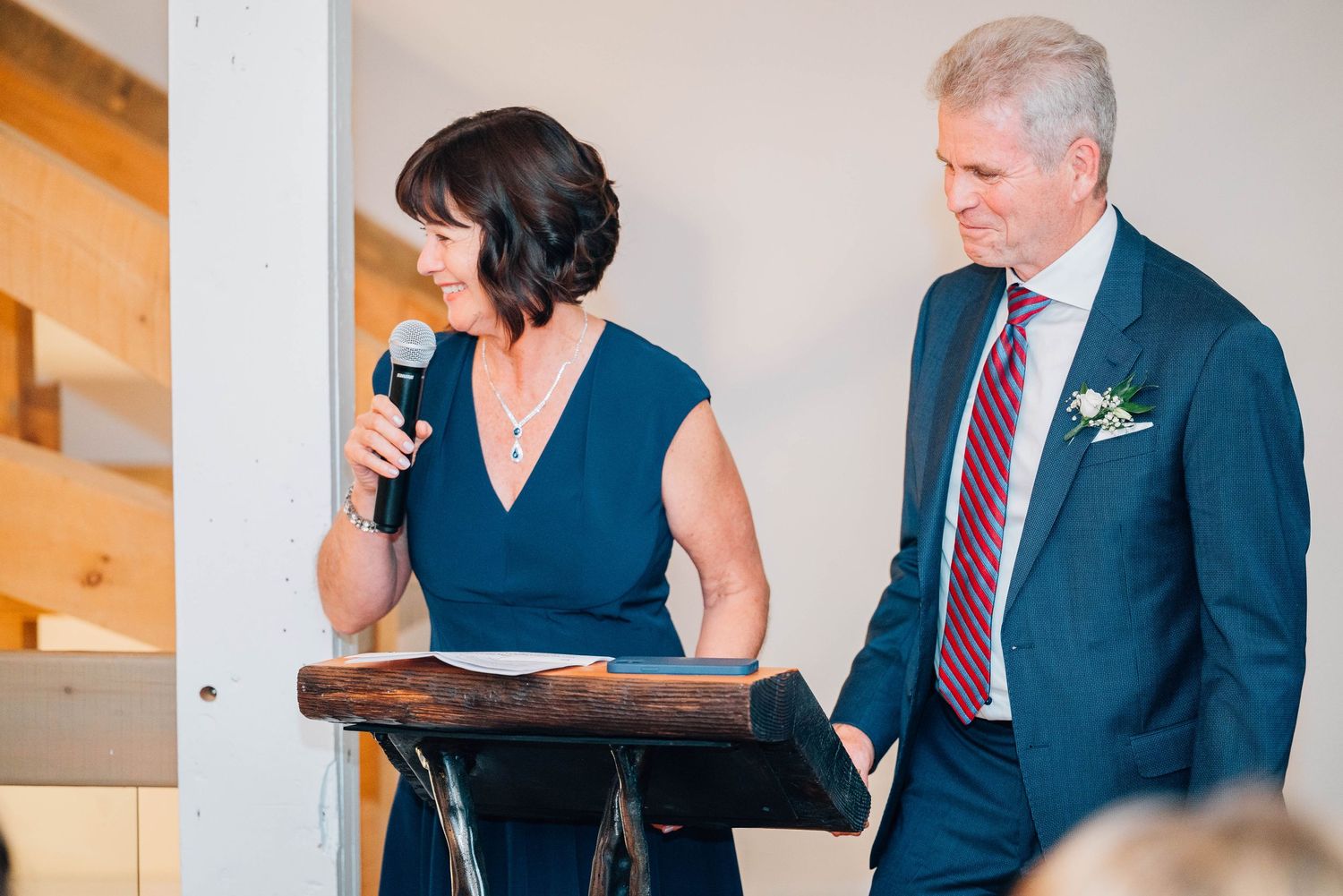 Mother of bride or groom speaking at wedding reception podium while man stands beside her.