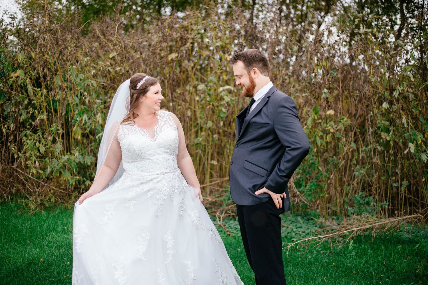 Bride and groom share a romantic glance outdoors on their wedding day, surrounded by lush greenery.