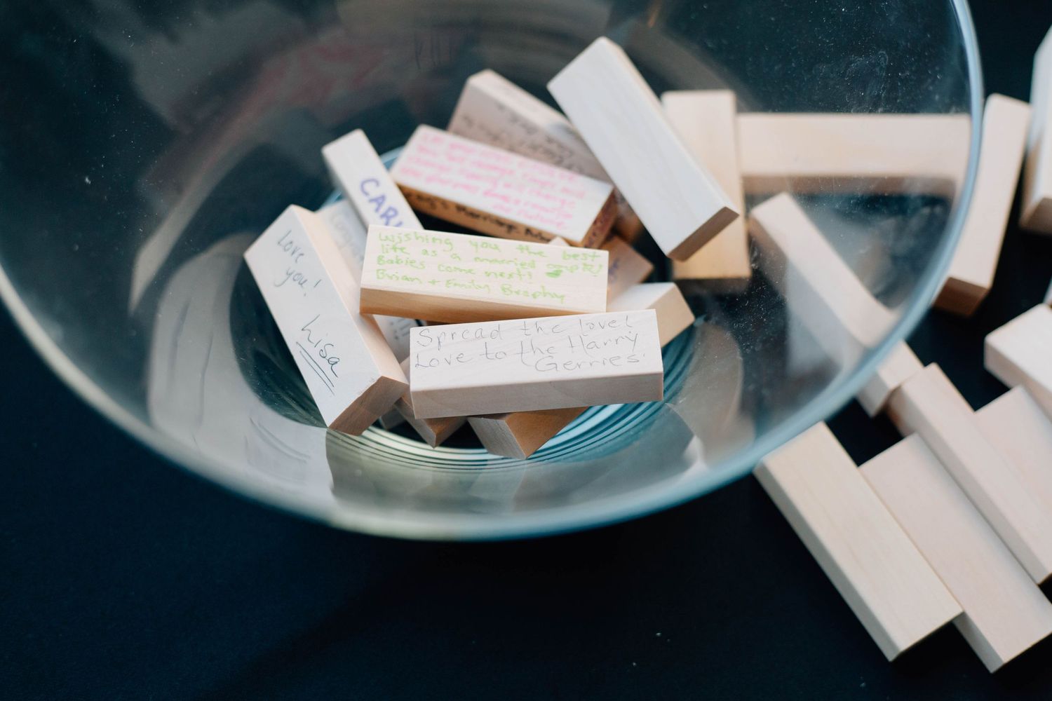 Close-up of personalized Jenga blocks with handwritten messages in a glass bowl at a wedding.