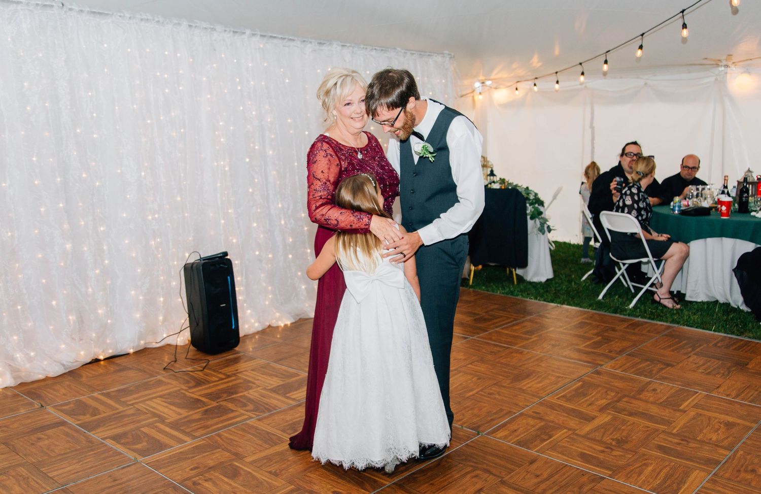 Groom dances tenderly with mother in elegant burgundy dress on wooden dance floor at reception.