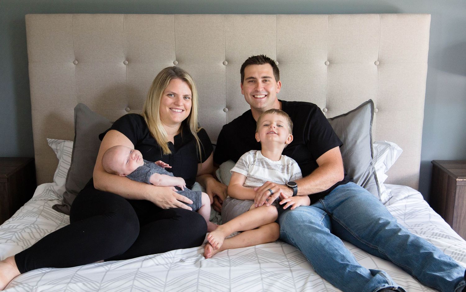 Happy family of four with newborn and toddler posing on a bed.