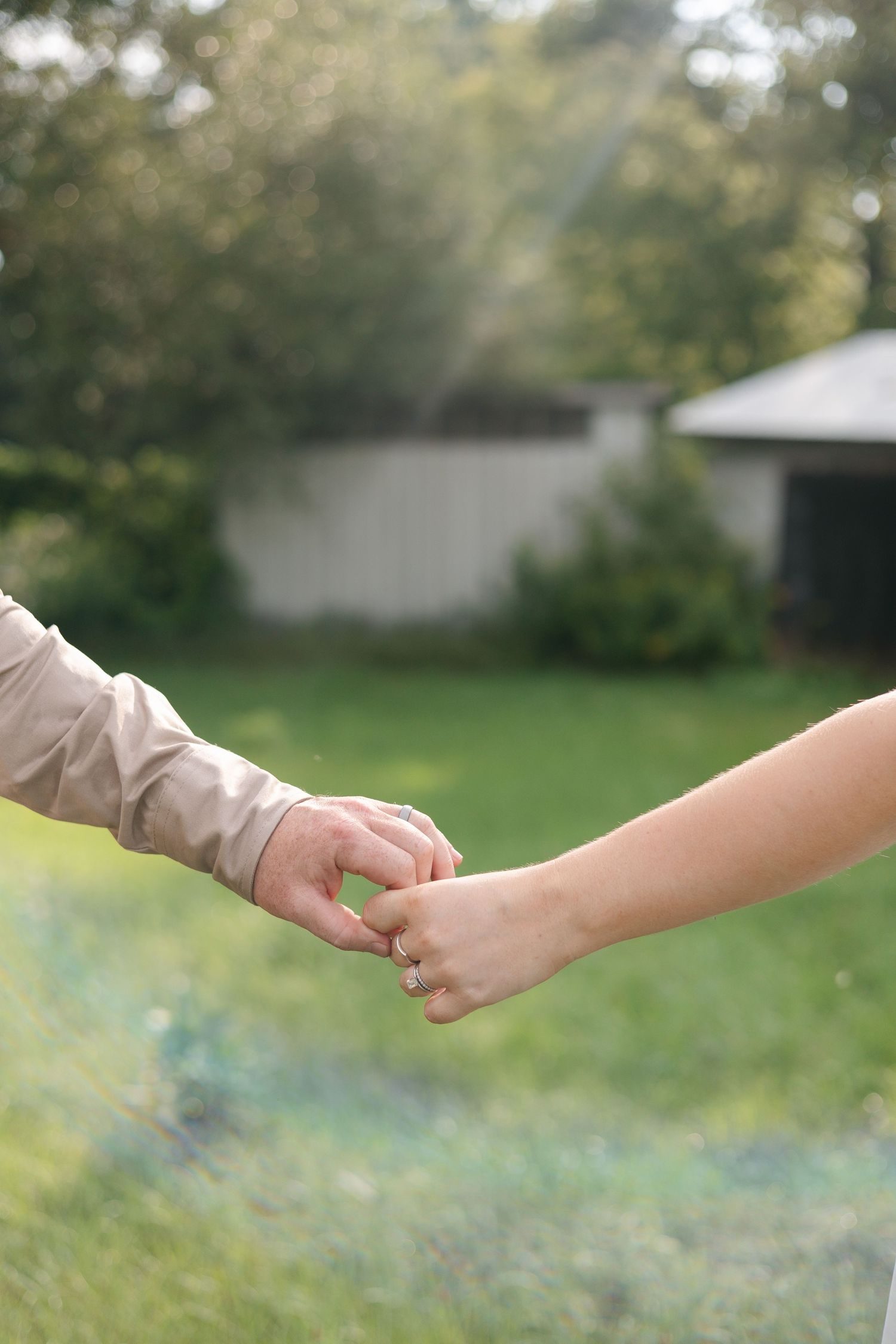 Two people holding hands with interlinked fingers outdoors in a green garden setting.