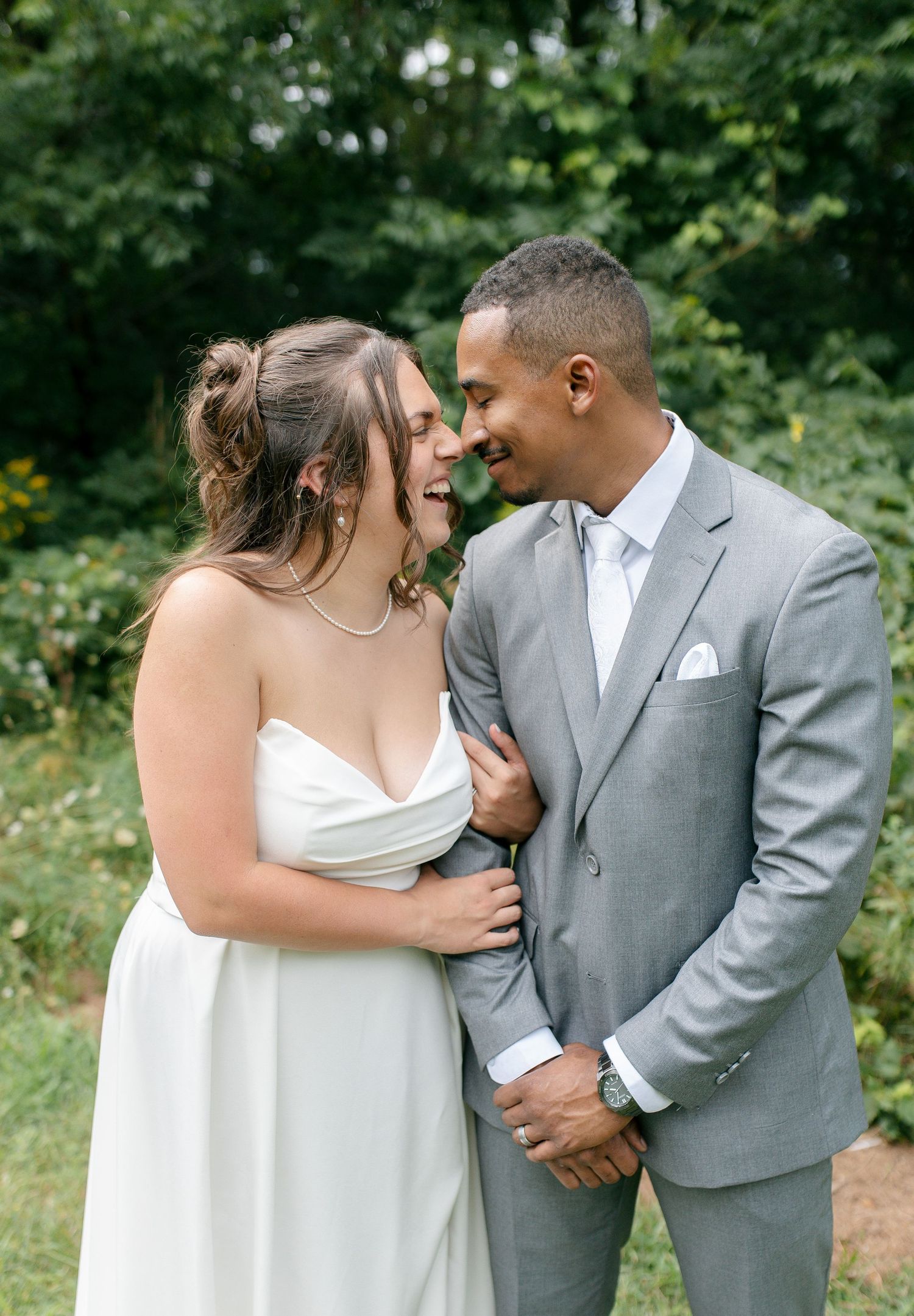 A bride and groom share a joyful moment in Woodstock Ontario, smiling at each other outdoors, she in white, he in a gray suit.