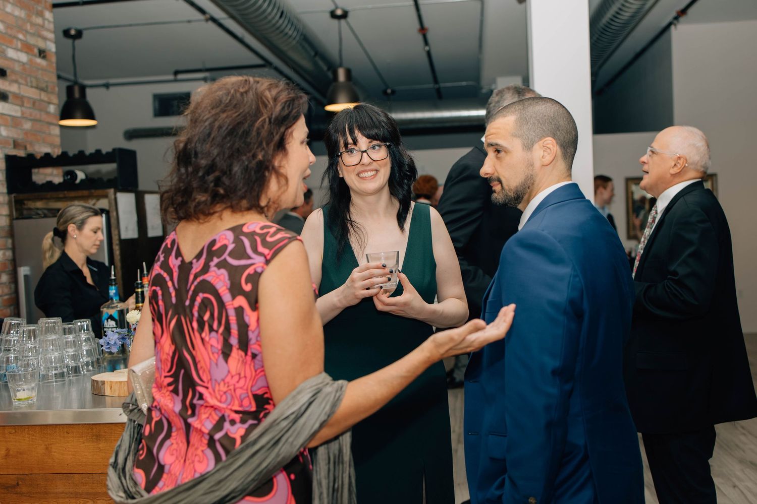 Wedding guests socializing at reception cocktail hour in rustic industrial venue with exposed brick walls.