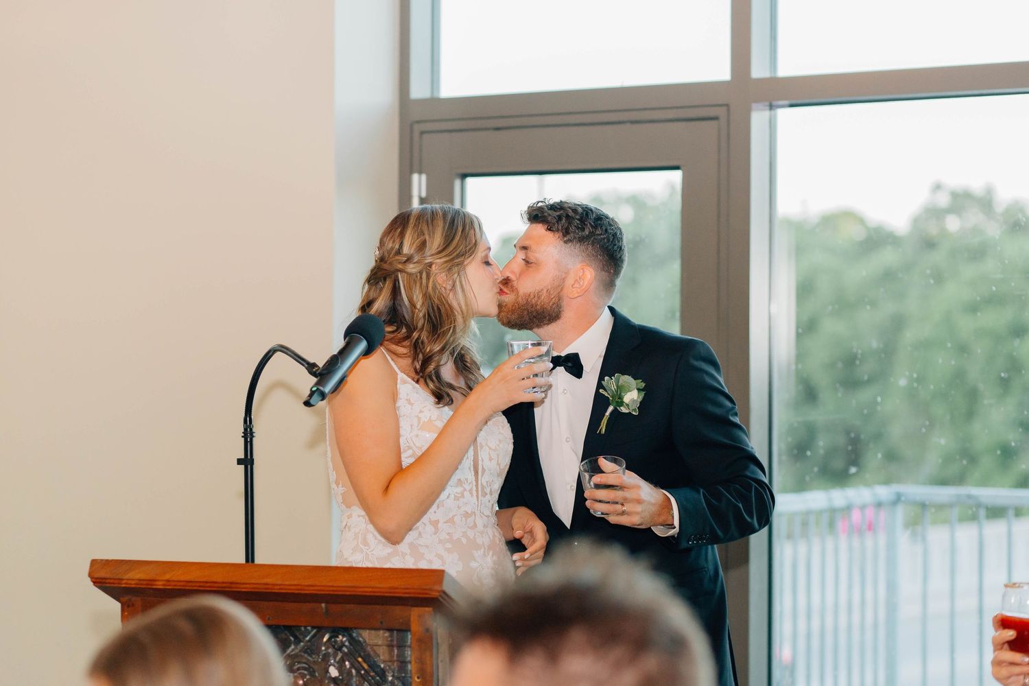 Bride and groom sharing a kiss at the podium during their wedding reception speech at Rivers Edge at the Arlington.