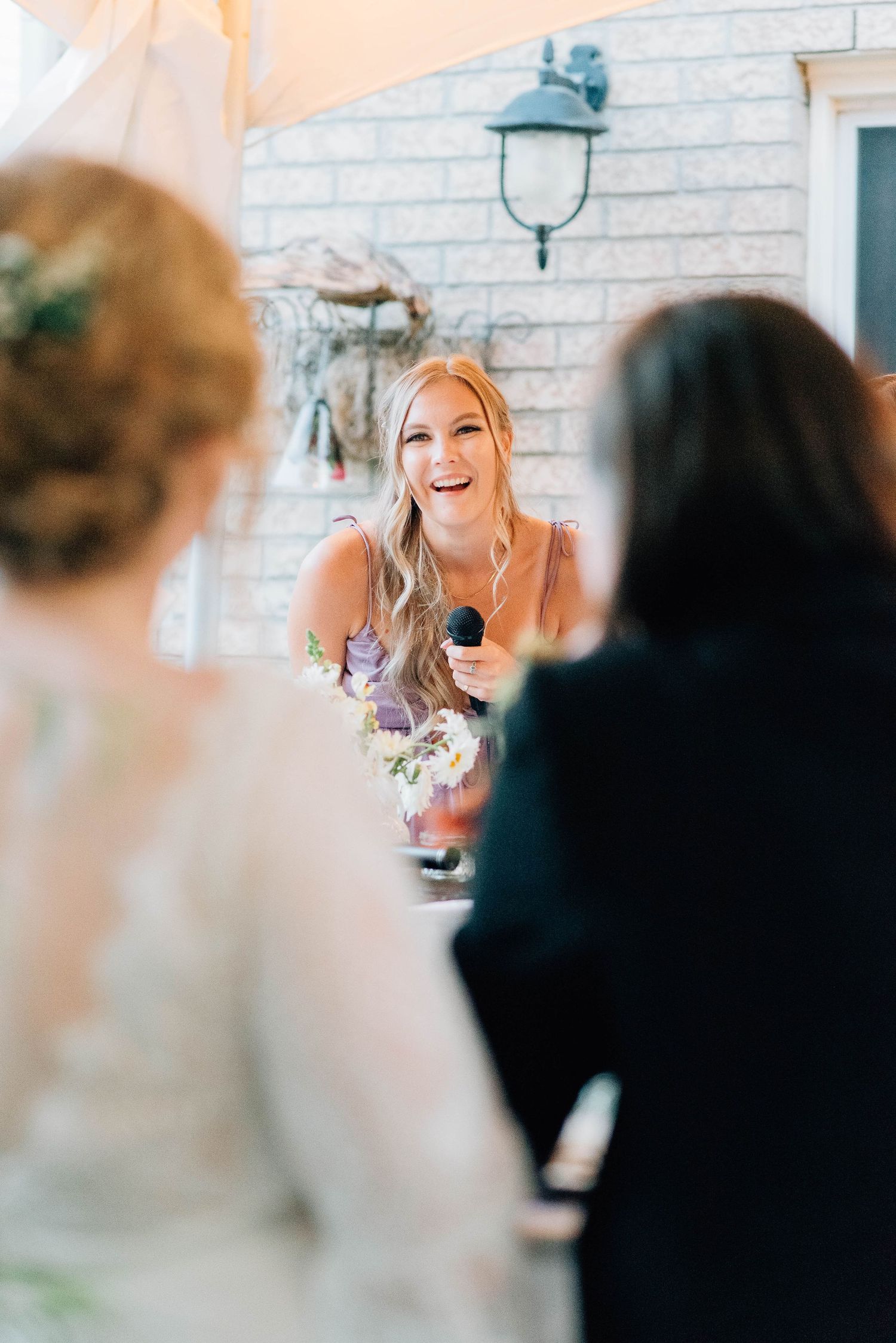Smiling bridesmaid in purple dress gives a speech holding a microphone at a wedding reception.