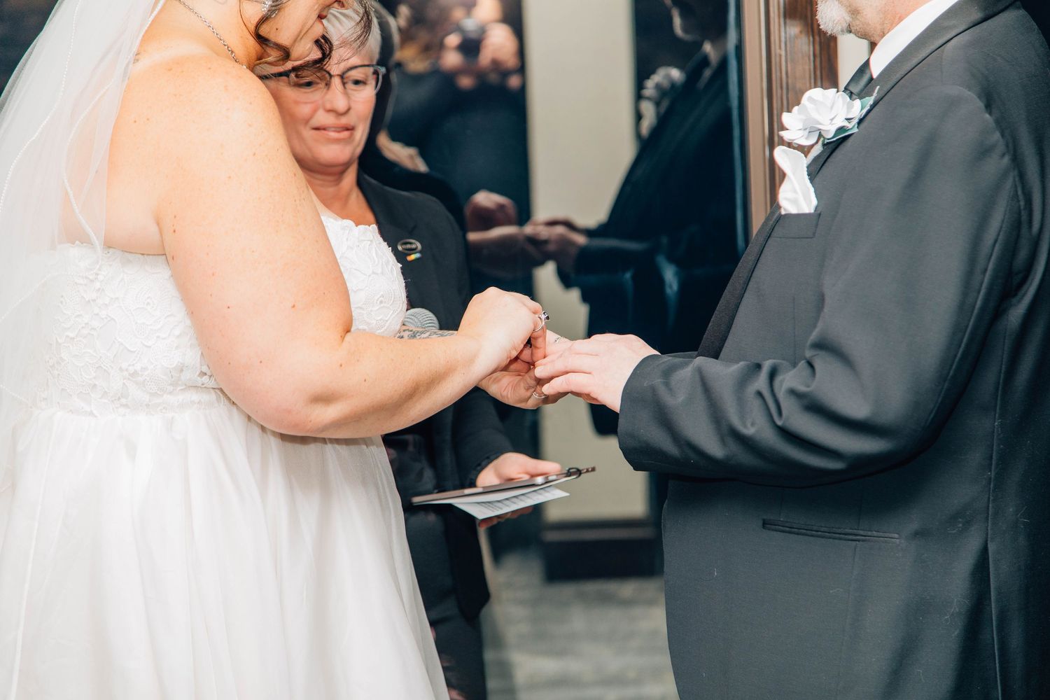 Groom places wedding ring on brides finger during intimate indoor wedding ceremony exchange of vows.