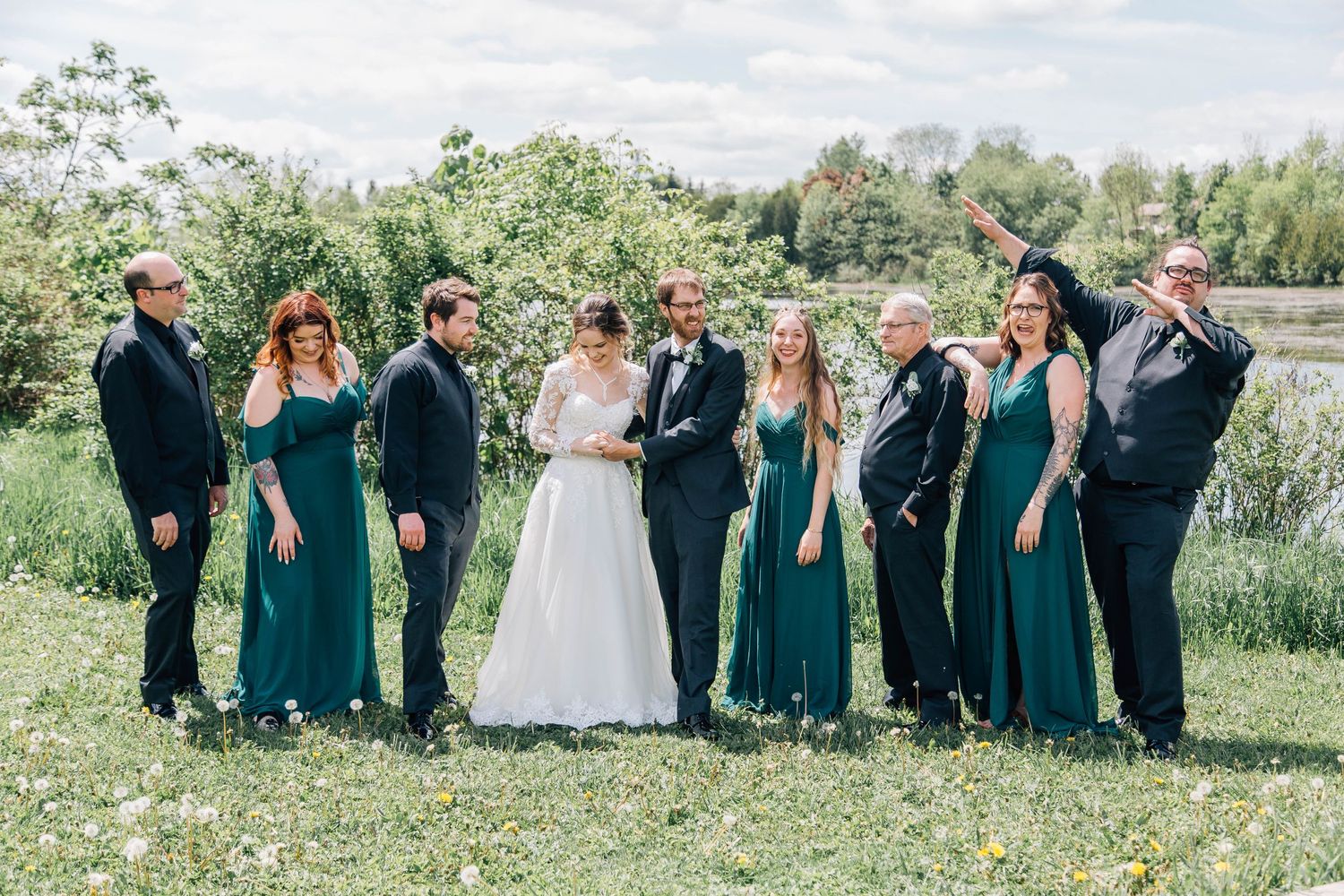 Wedding party laughing together outdoors, bridesmaids in emerald green dresses with bride and groom centered.