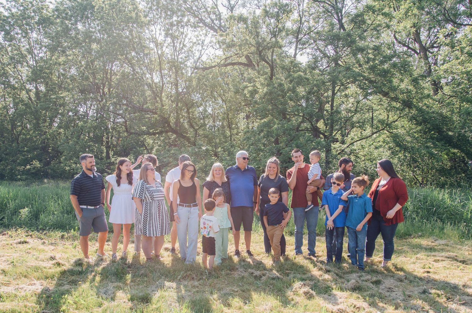 Large extended family group portrait standing together in a lush green outdoor setting on a sunny day.