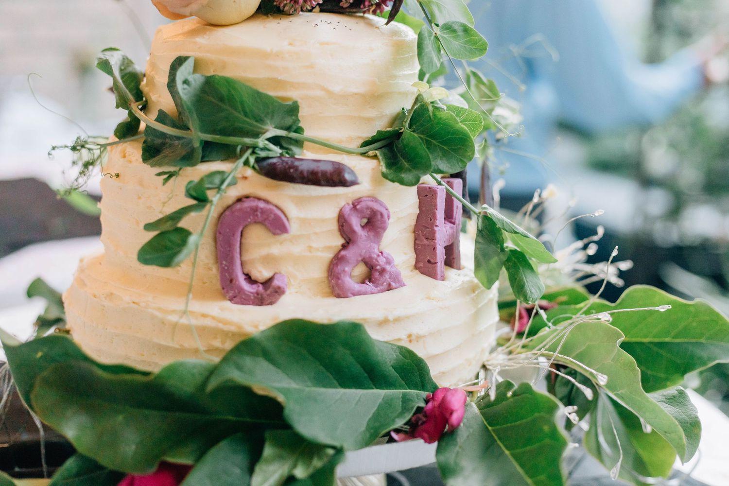 Two-tier rustic wedding cake decorated with C&H initials, greenery, and fresh flowers.