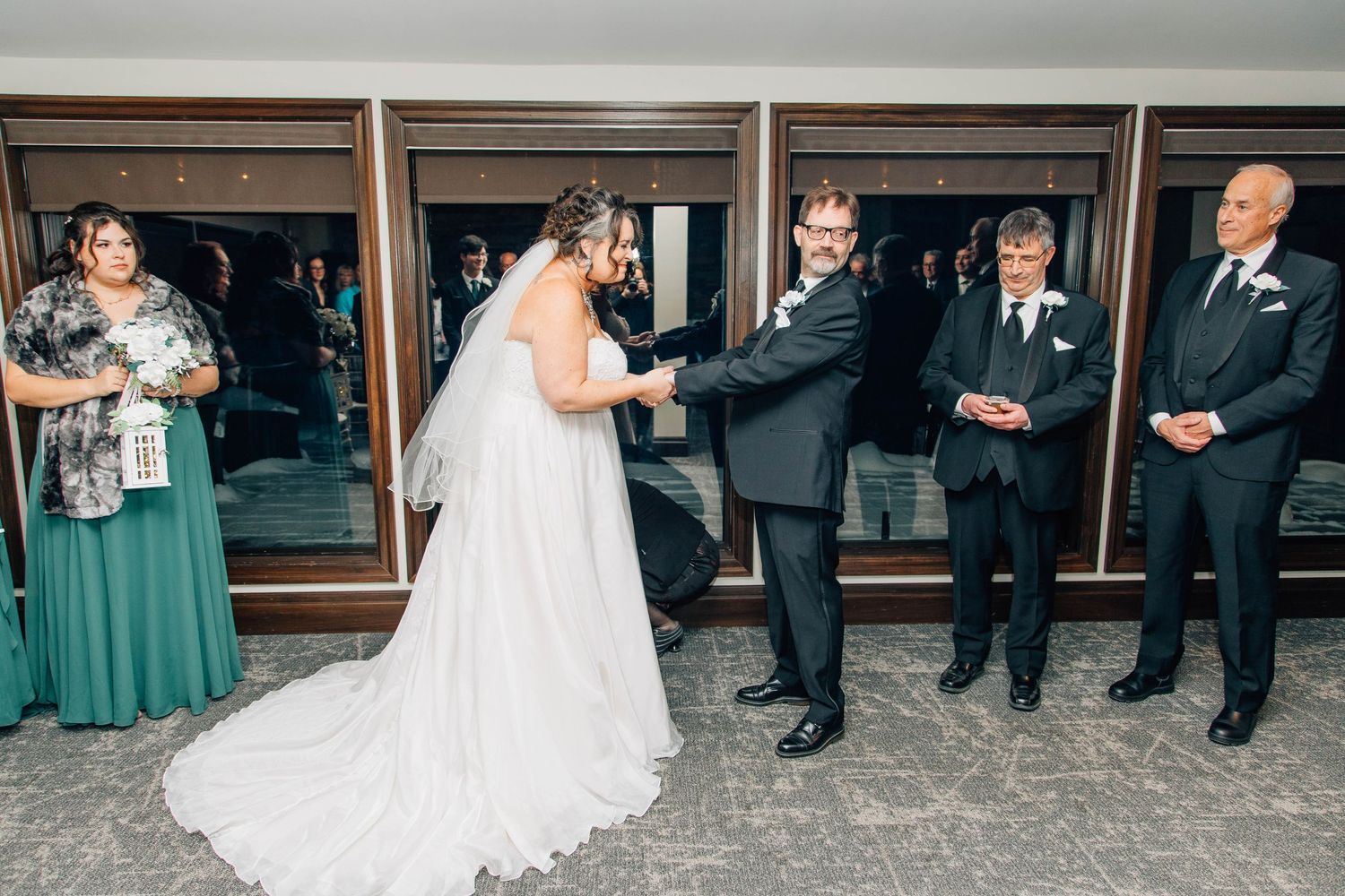 Bride in white gown and veil joins hands with groom during wedding ceremony before officiant and guests.