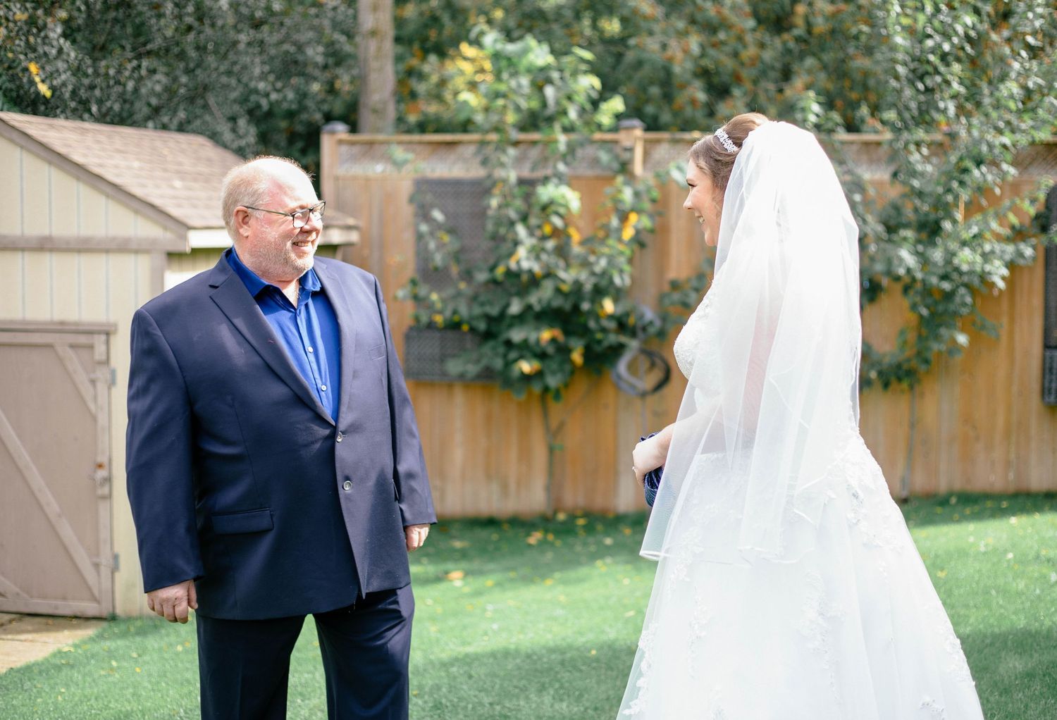 Father in navy suit reacting with emotion during first look at bride in white lace gown and veil.