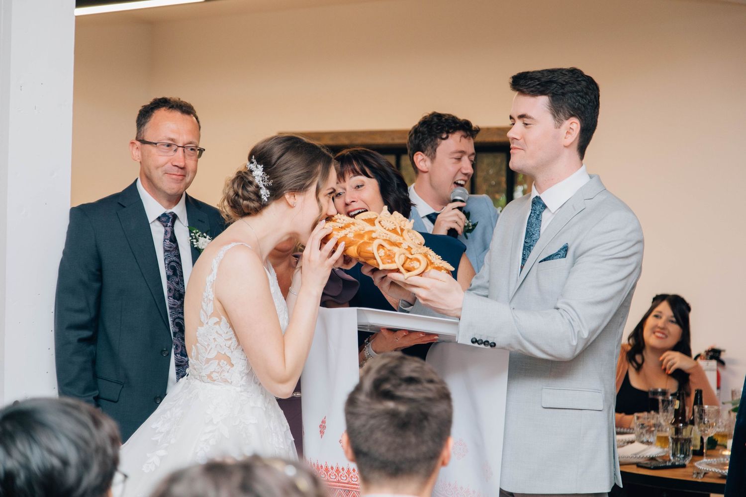 Bride and groom sharing a traditional bread breaking ceremony with smiling wedding guests.