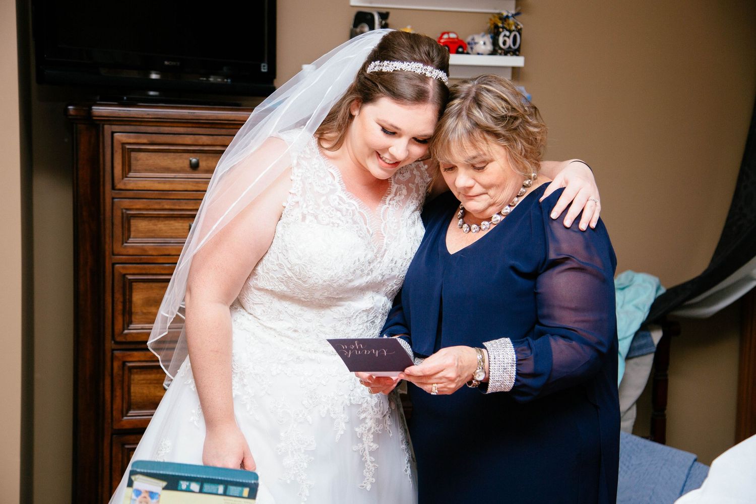 Bride in white lace gown and veil sharing a tender moment reading a card with elderly woman.