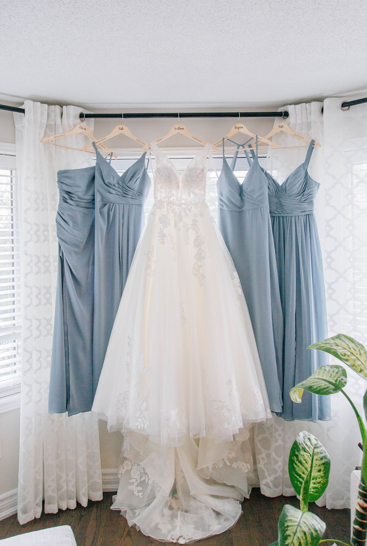 White lace wedding gown flanked by four dusty blue bridesmaid dresses on hangers.