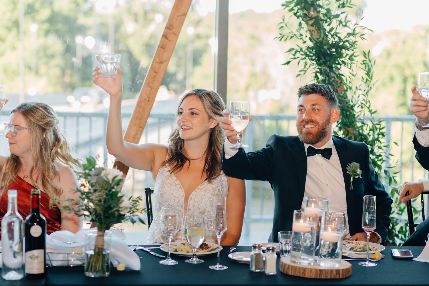 Bride and groom raise champagne glasses in a toast at candlelit wedding reception table with lush greenery in Paris Ontario.