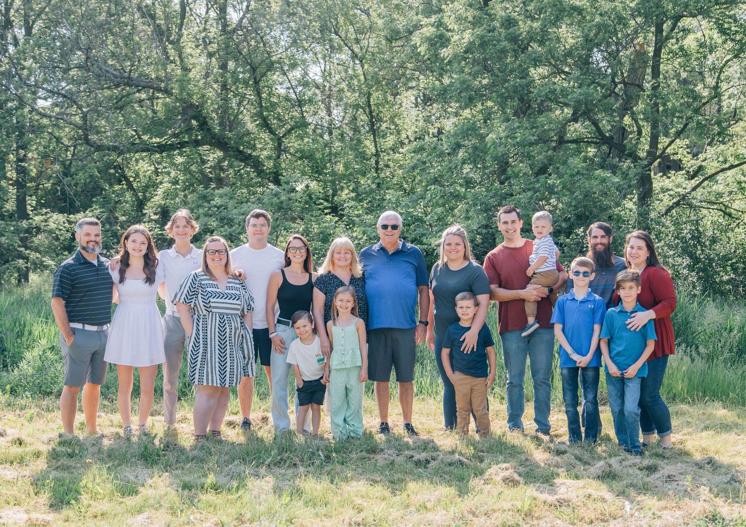 Large extended family group portrait standing together in green outdoor park setting.