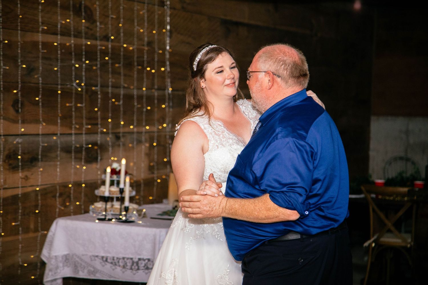 Bride sharing a special father-daughter dance at wedding reception near decorated cake table.